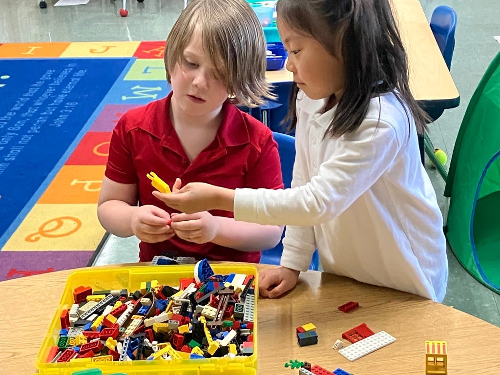 Two children at a table building with colorful toy bricks