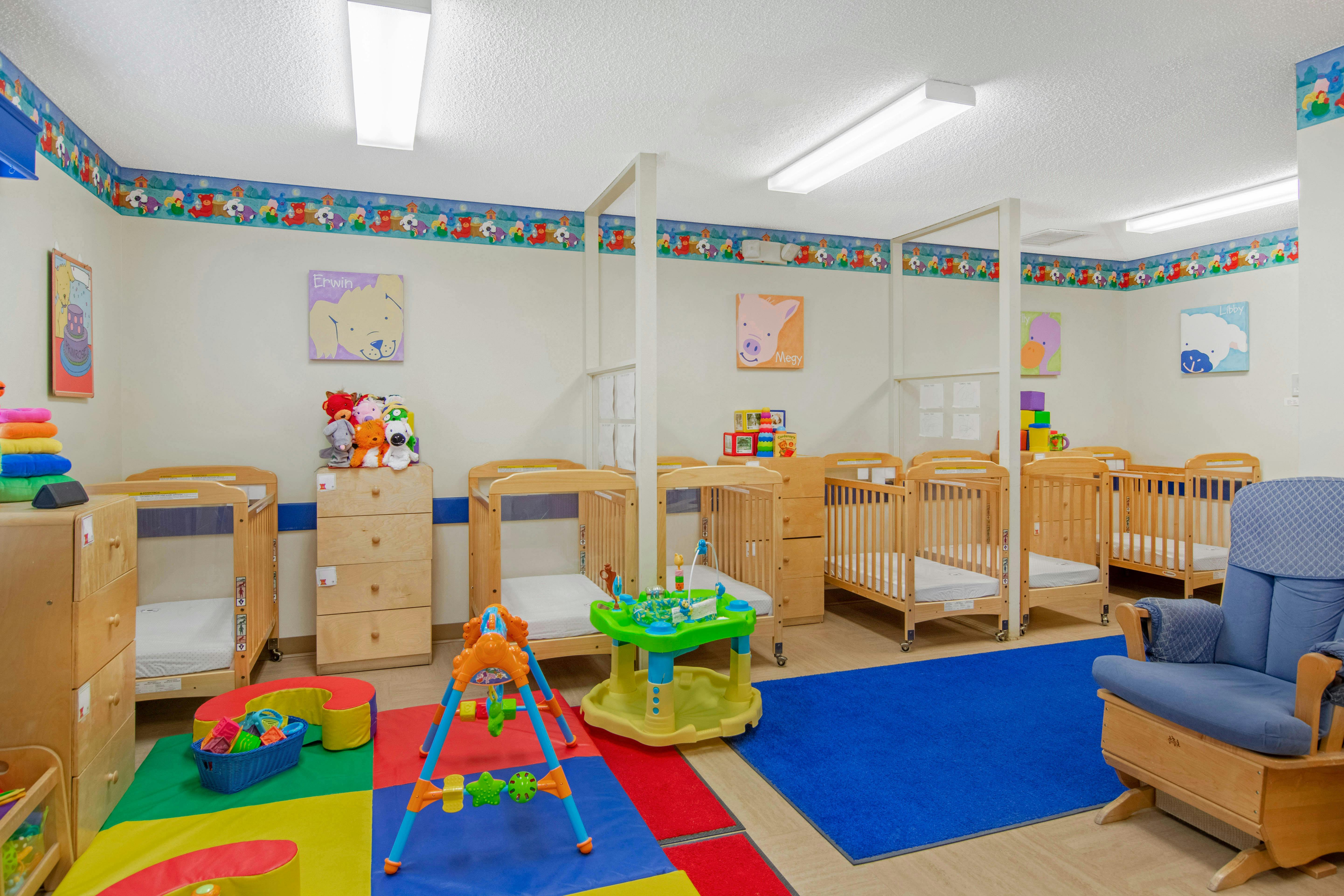 Cribs in a daycare room with a colorful play mat and blue rug