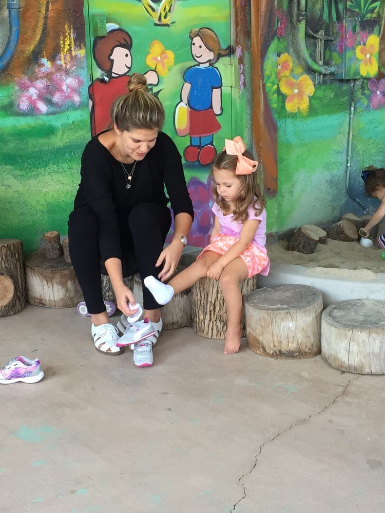 Person putting a shoe on a child sitting on a tree stump