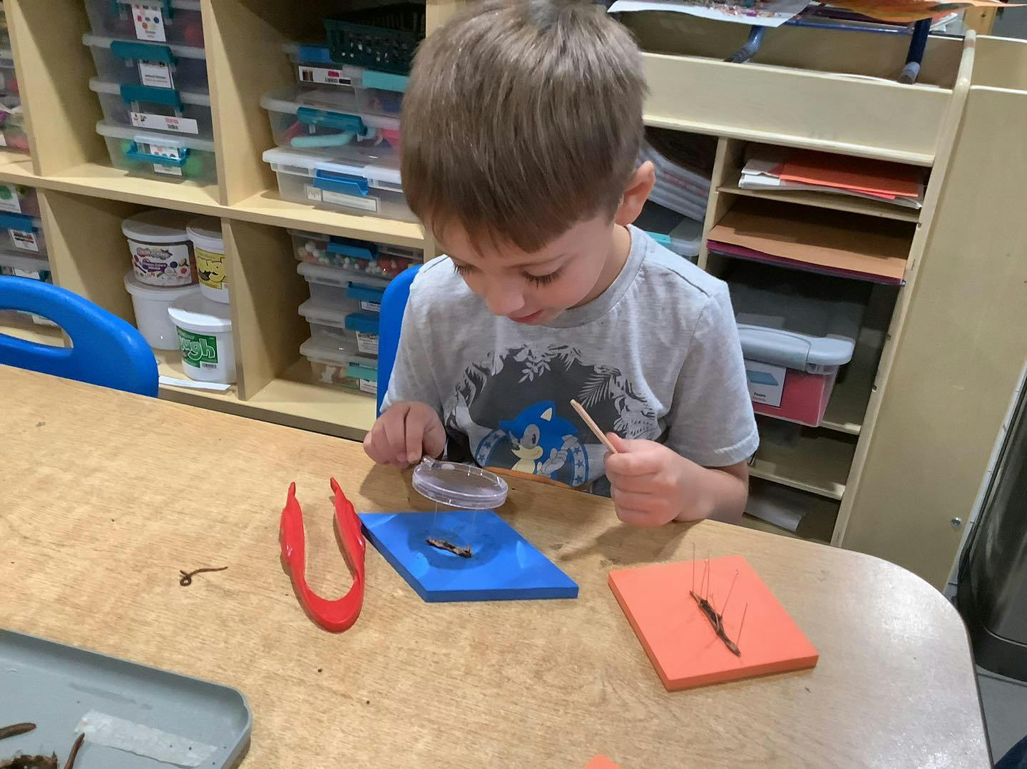 Child examining objects on a table with a magnifying glass and stick