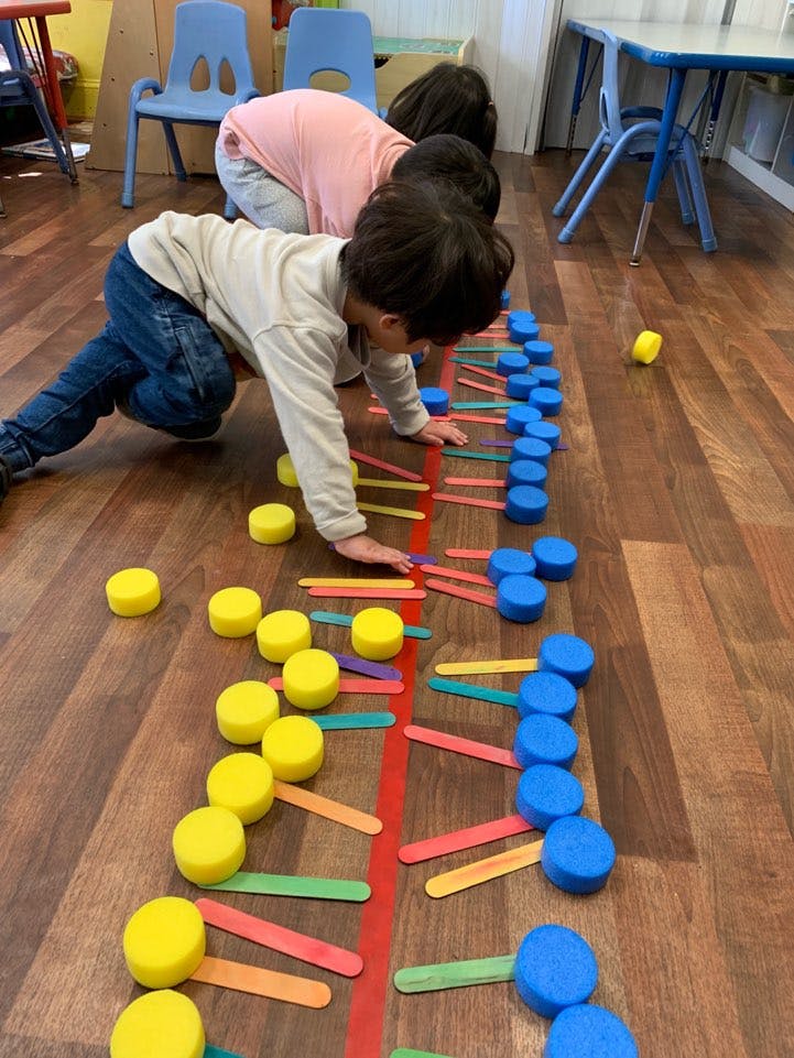 Two children on the floor playing with colorful craft sticks and foam circles