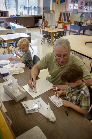 Adult and child writing on paper at a table in a classroom