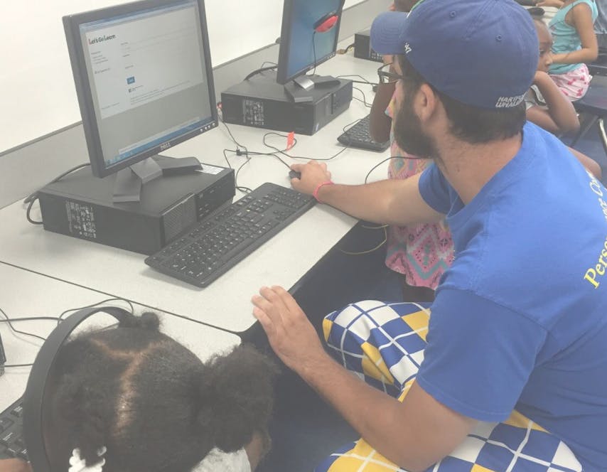 Person in blue shirt and cap helping a child at a computer