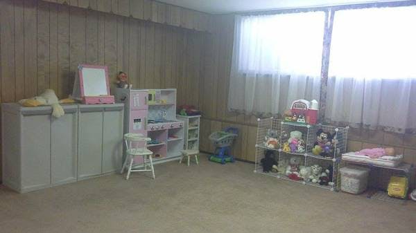 Playroom with toy kitchen, shelves of toys, and windows with windows in front of windows