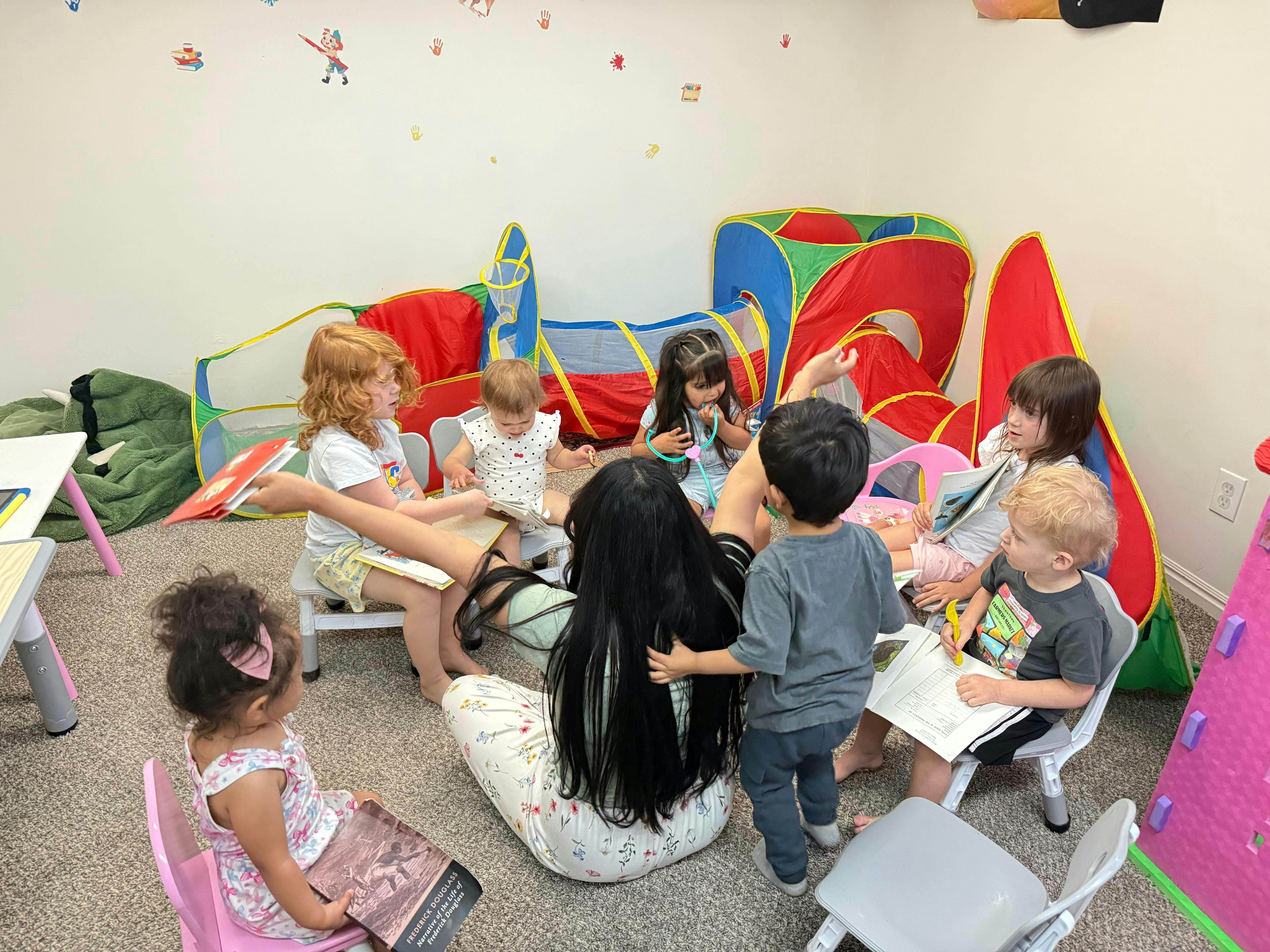 Group of children sitting with an adult in a playroom with a play tent