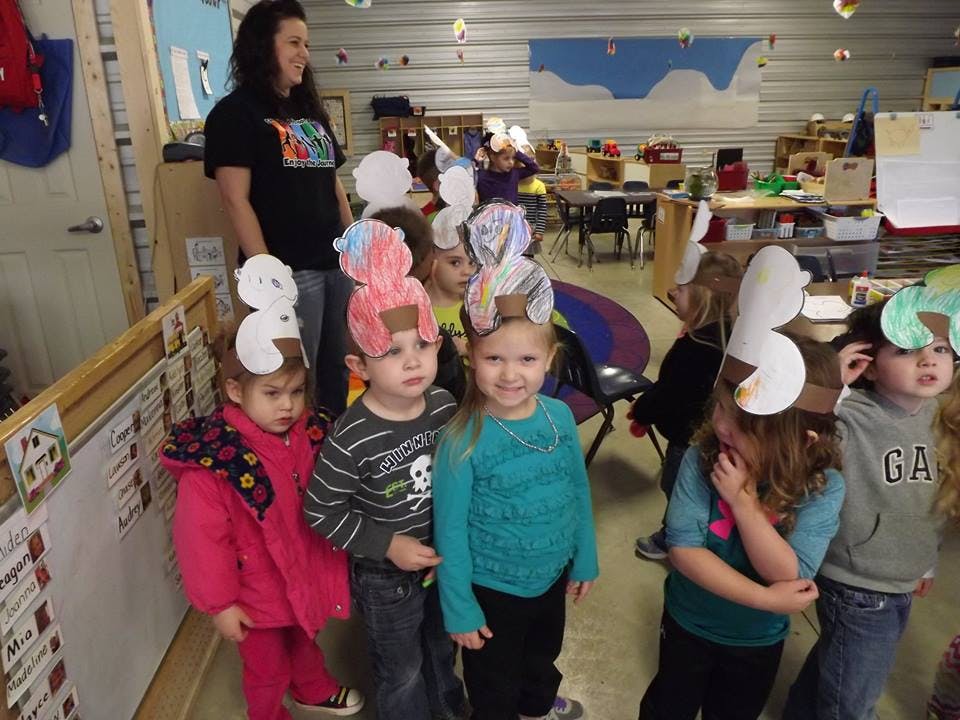Person standing behind children wearing paper hats in a classroom