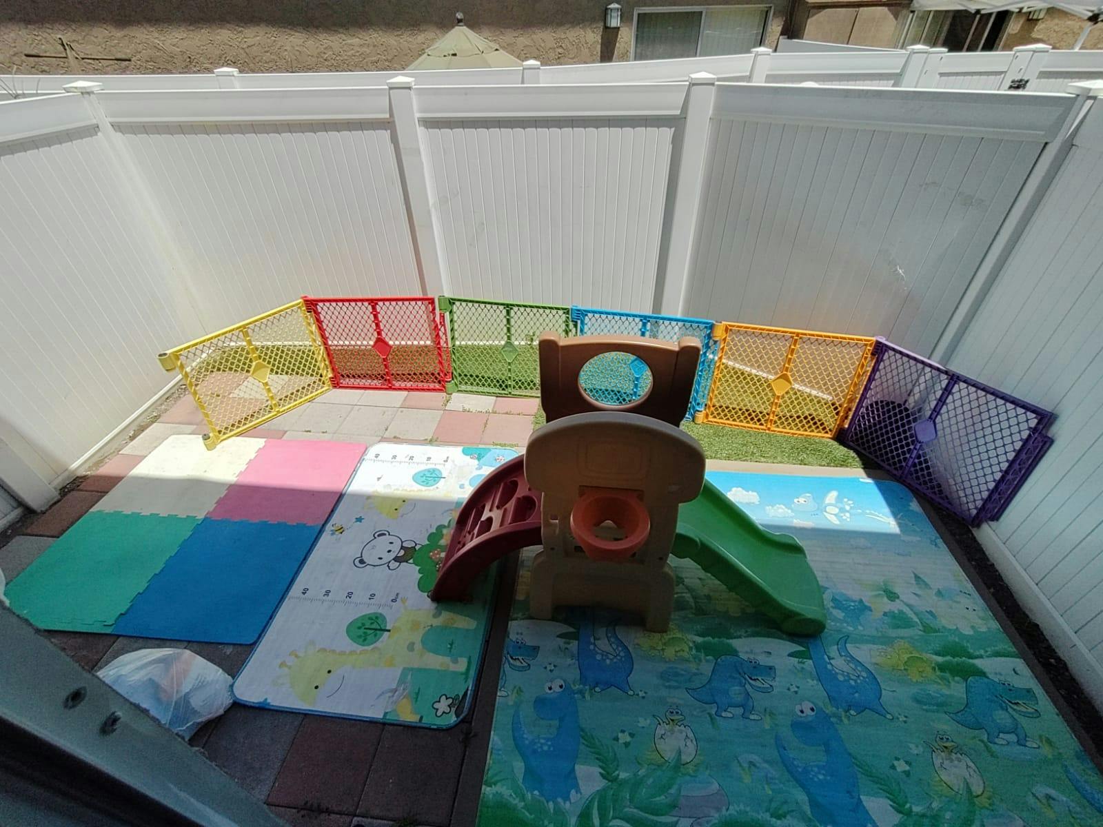 Play area with colorful mats, a small slide, and a playpen