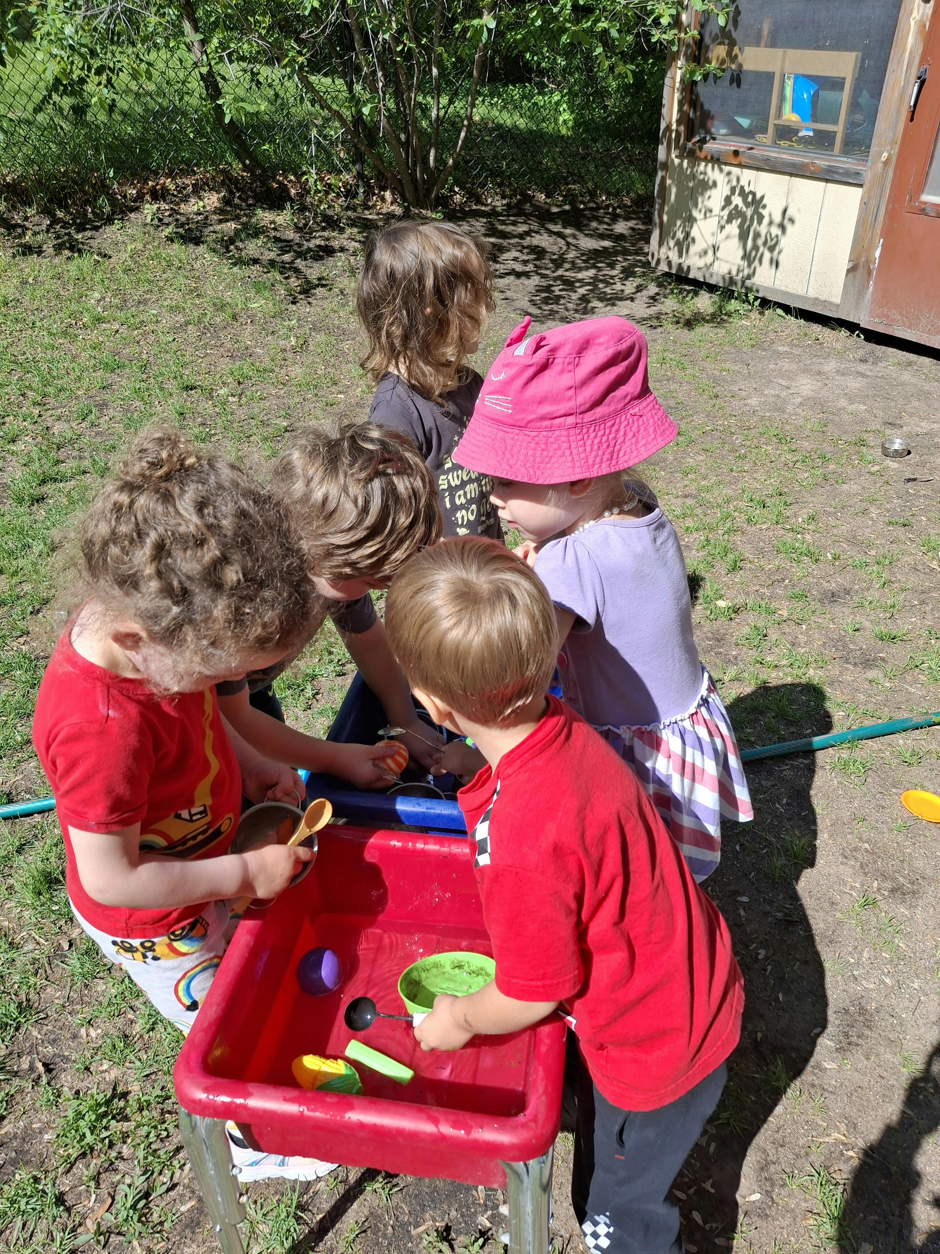 Children playing with a red water table outdoors