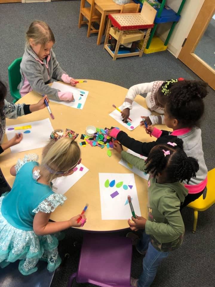 Children sitting around a table doing crafts with paper and art supplies