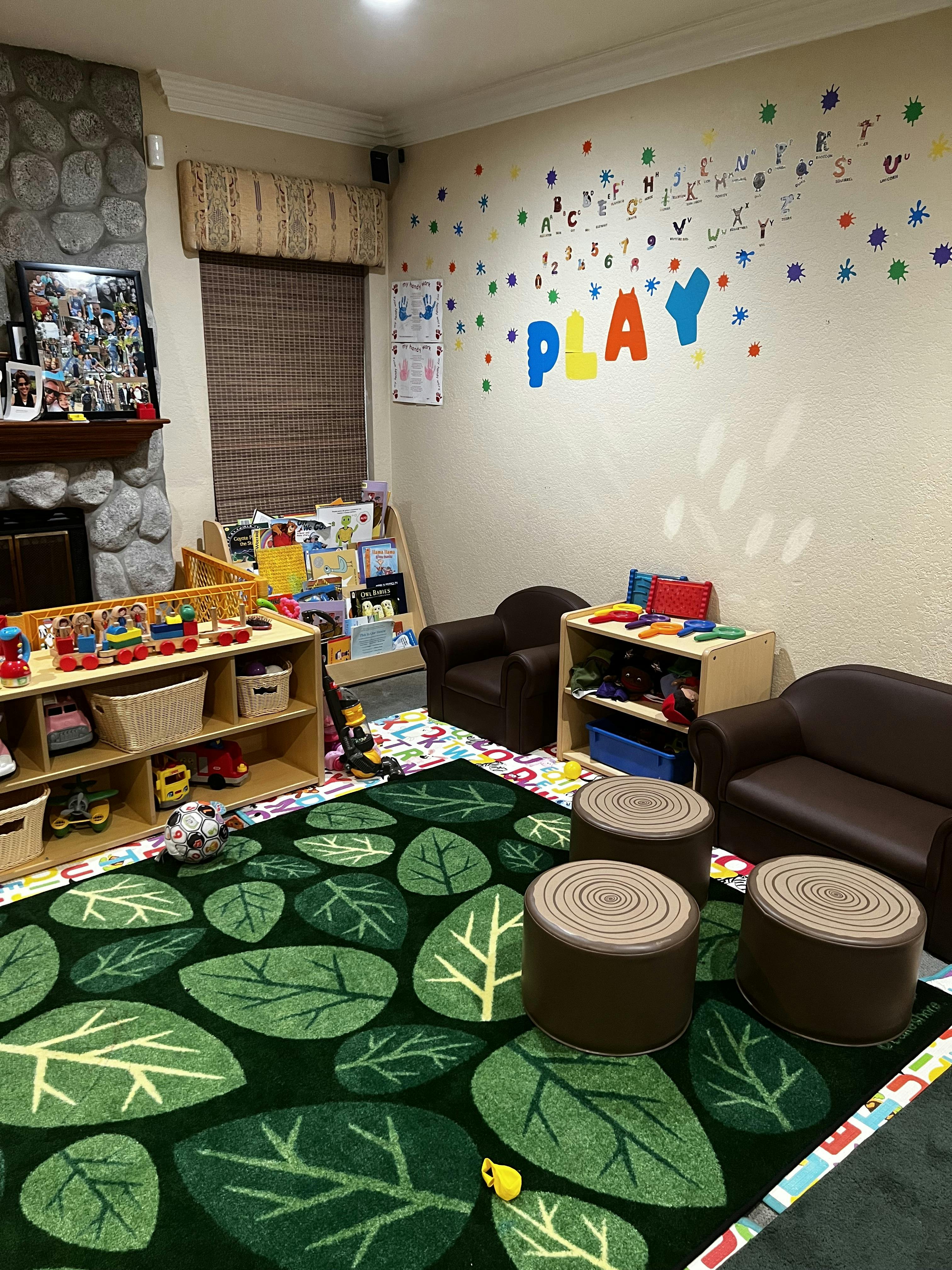 Children's play area with a leaf-patterned rug and the word "PLAY" on the wall