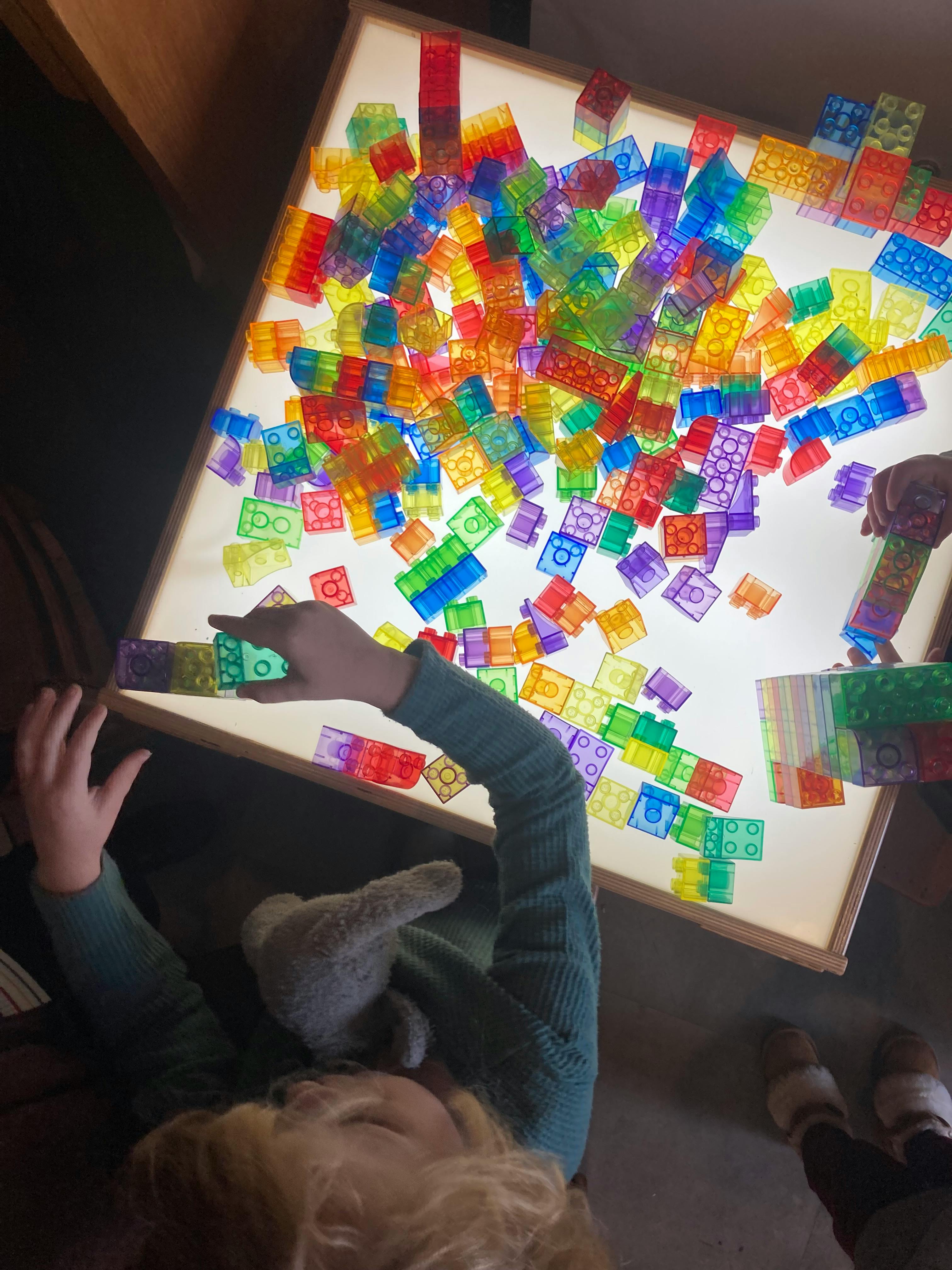 Child playing with colorful translucent building blocks on a light table