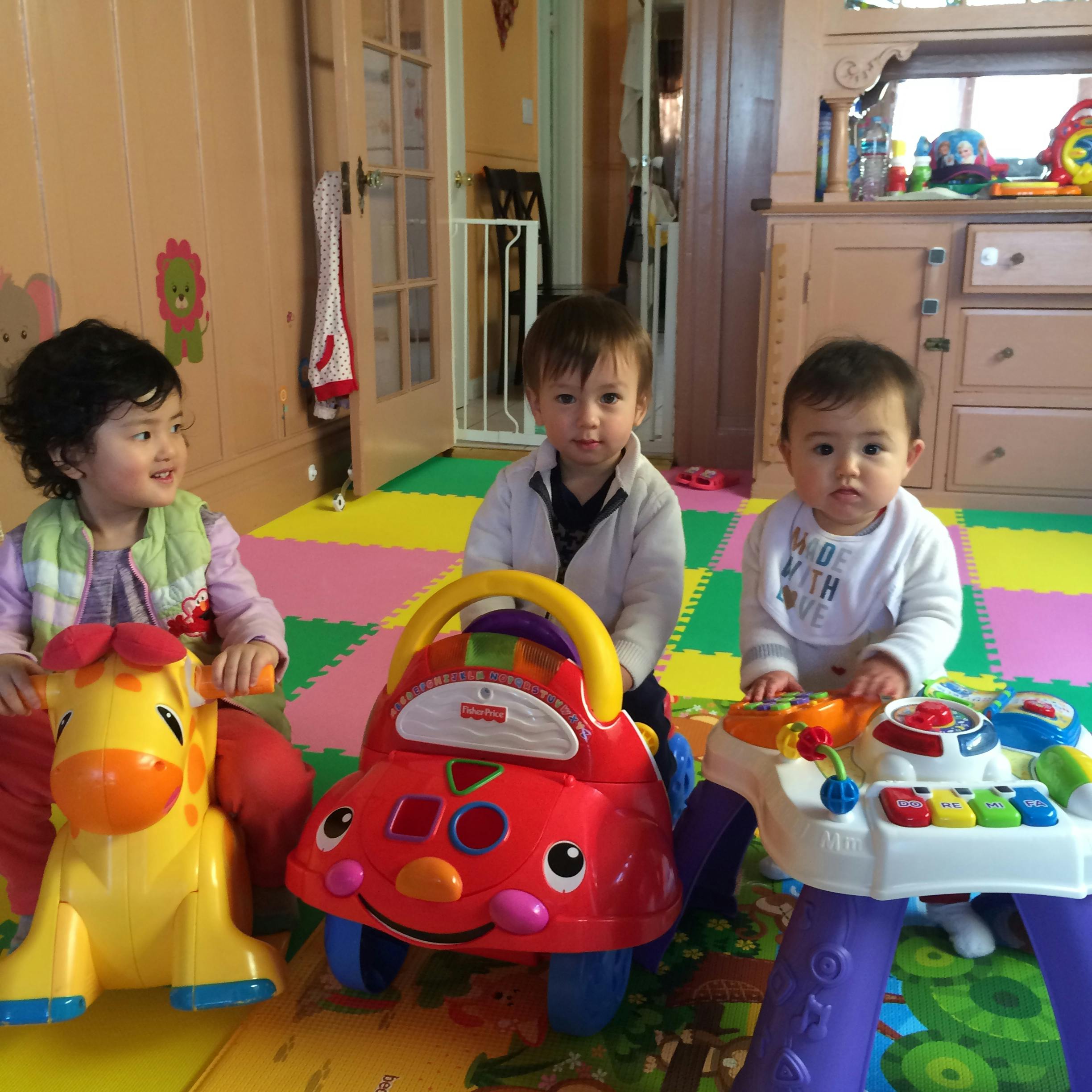 Three children playing with toys on a colorful mat