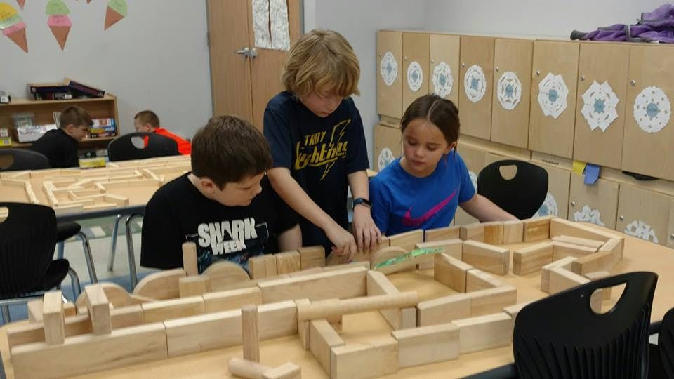 Three children building with wooden blocks in a classroom