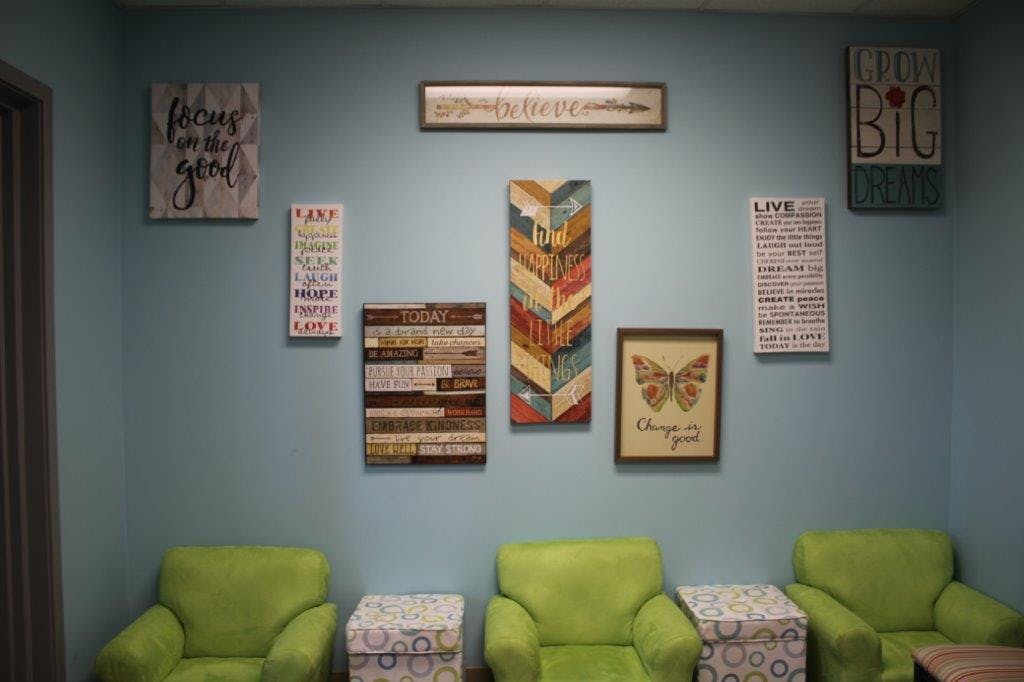 Wall decorated with various framed art and signs above green chairs