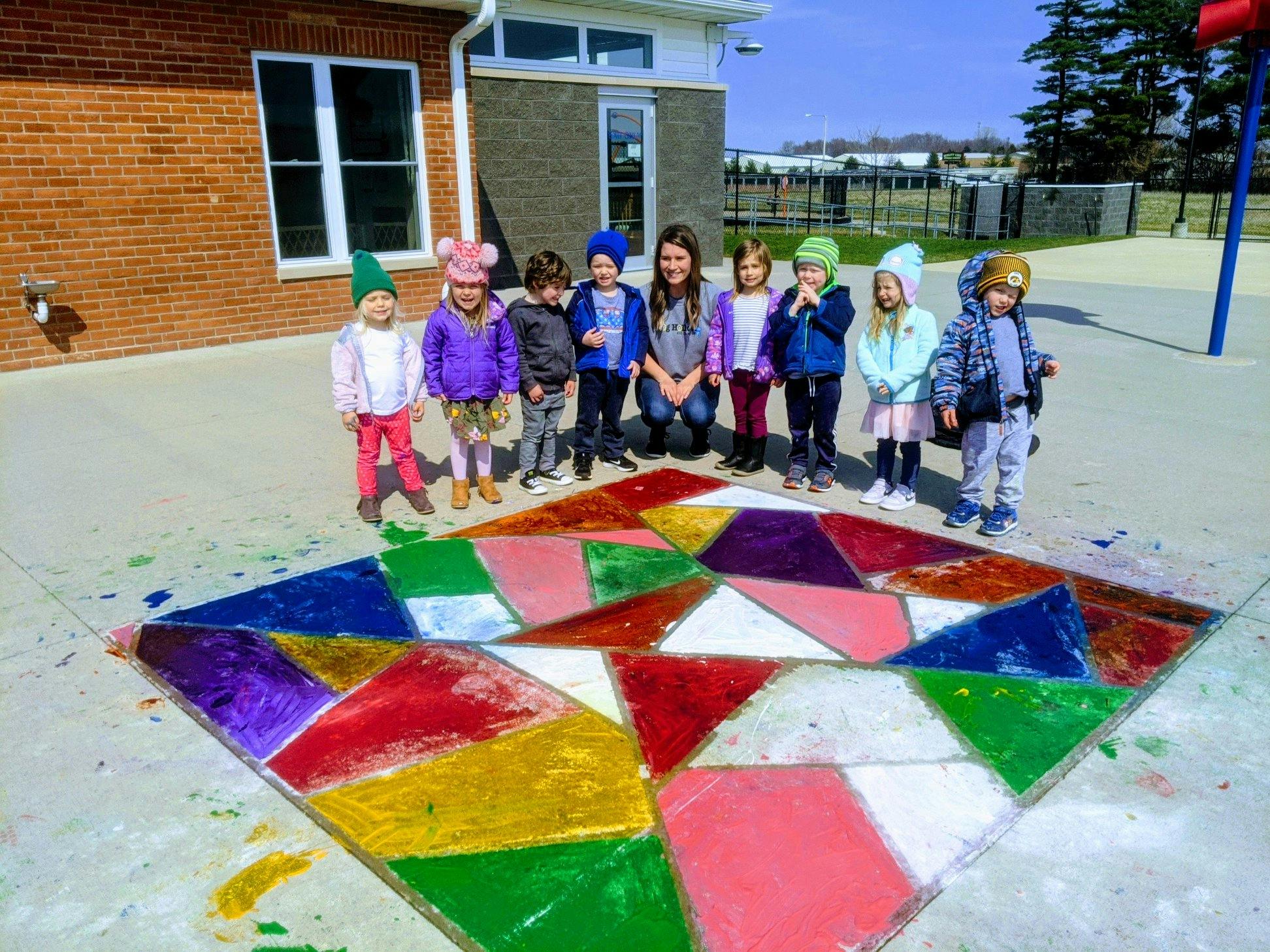 Adult and children standing around a colorful geometric pattern on the ground