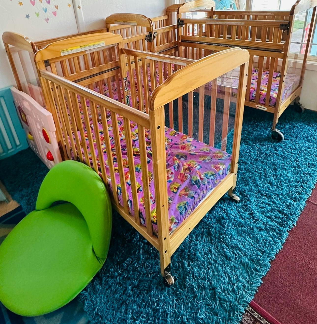 Multiple wooden cribs with purple bedding on a blue rug