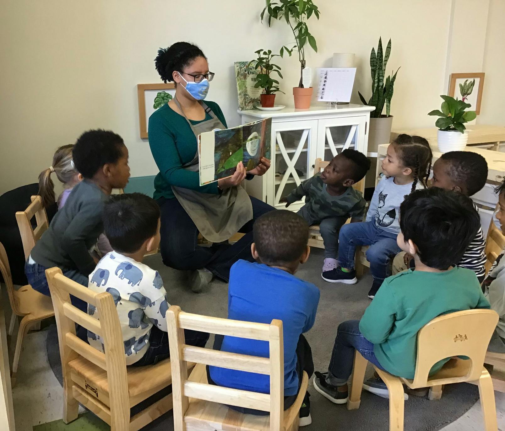 Person in mask reading a book to children in a classroom