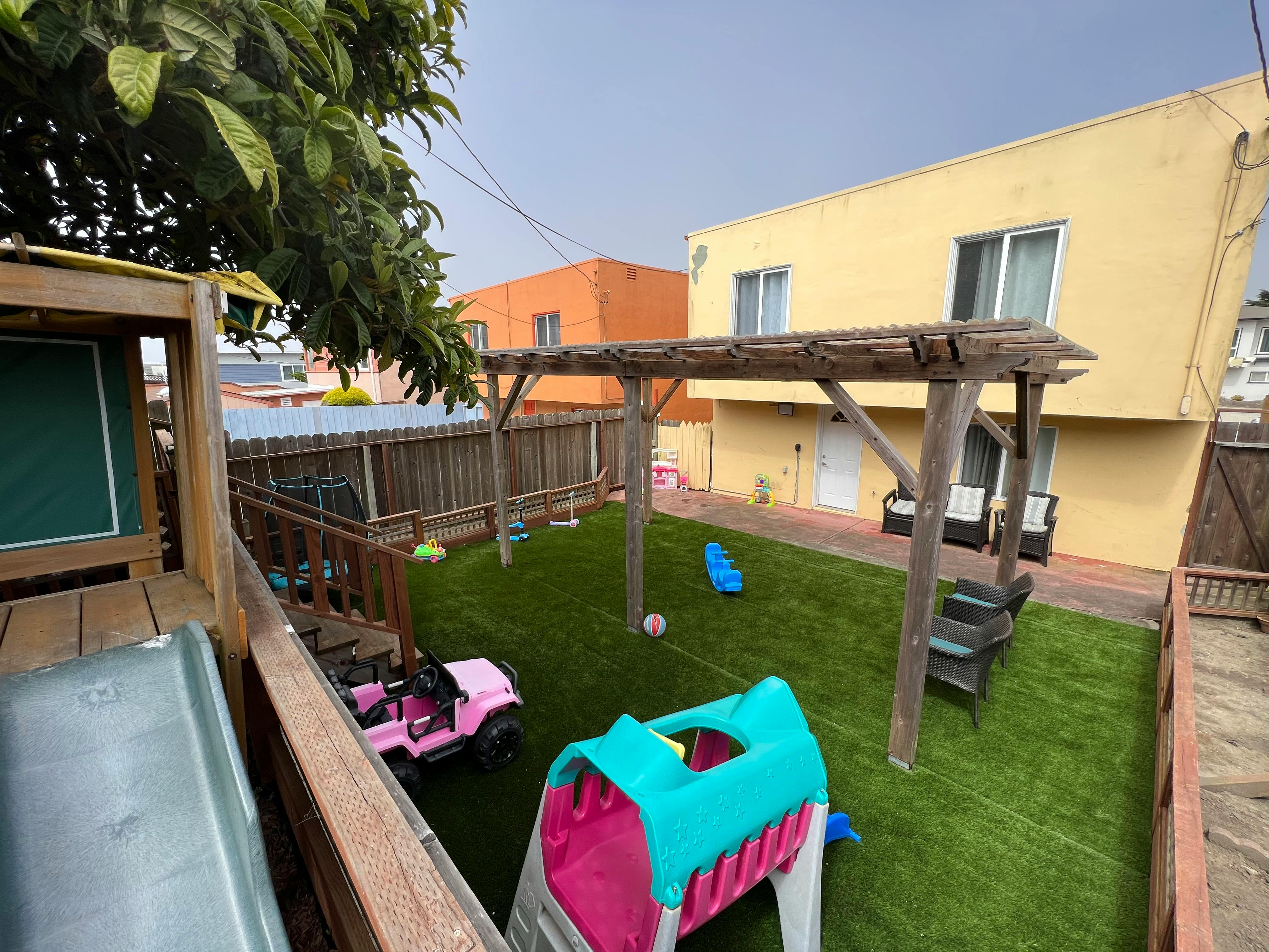 Backyard with artificial turf, play structures, and a pink toy car