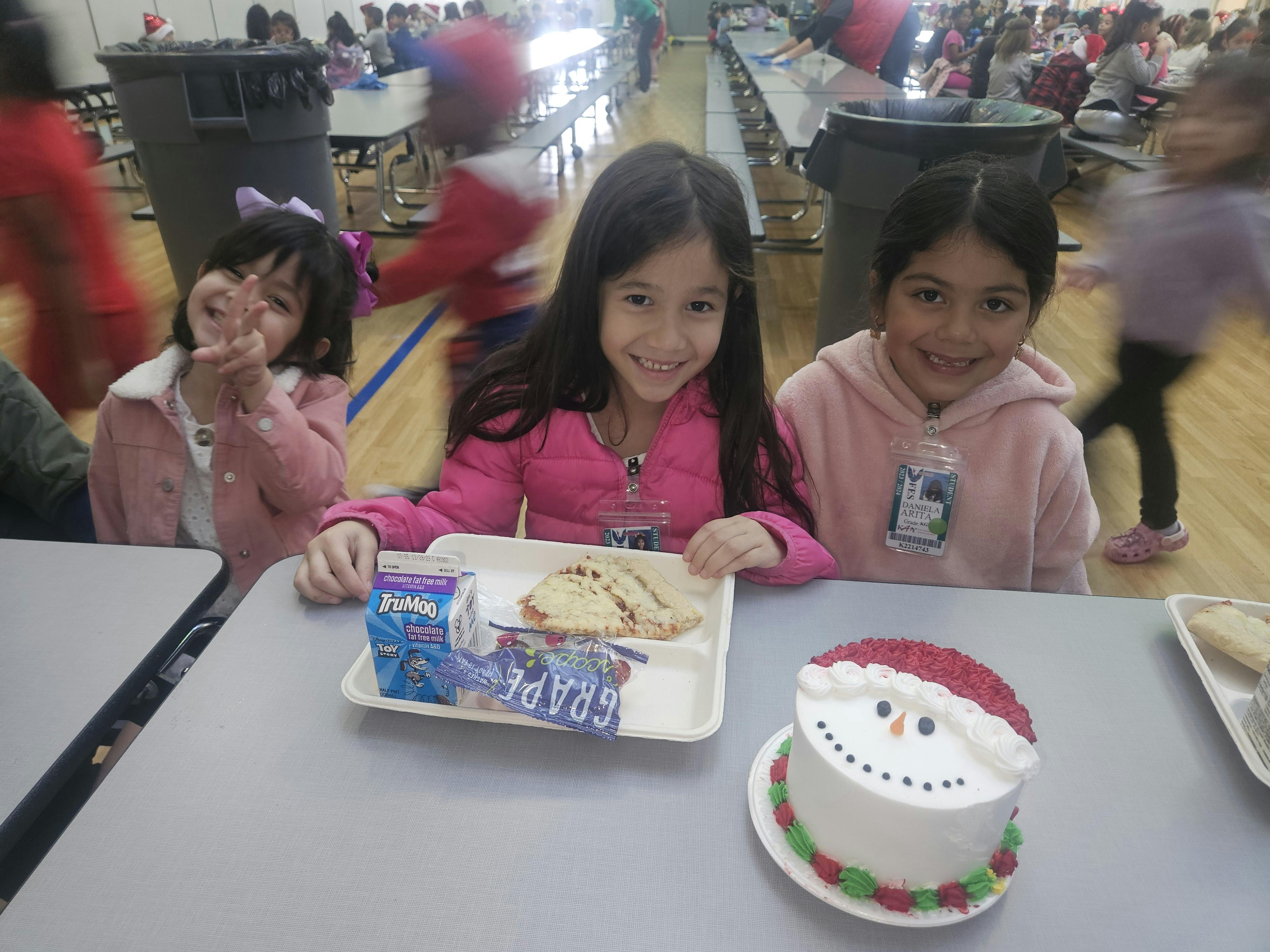 Three children sitting at a table with food trays and a snowman cake