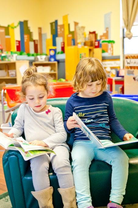 Two children sitting on a couch reading books in a classroom