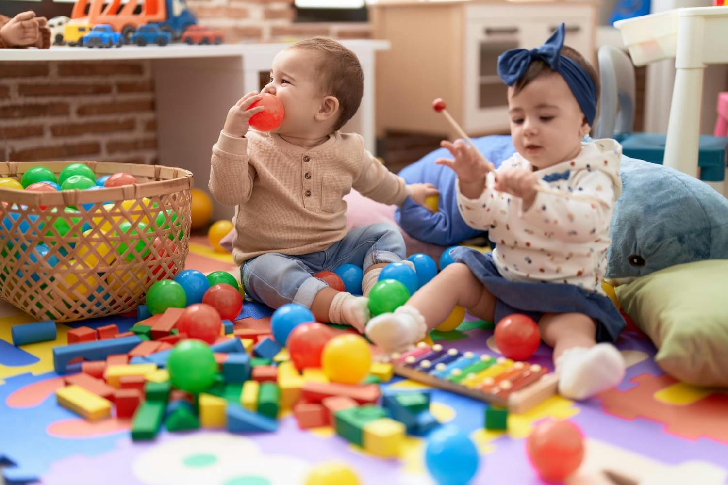 Two children sitting on the floor surrounded by colorful blocks and balls