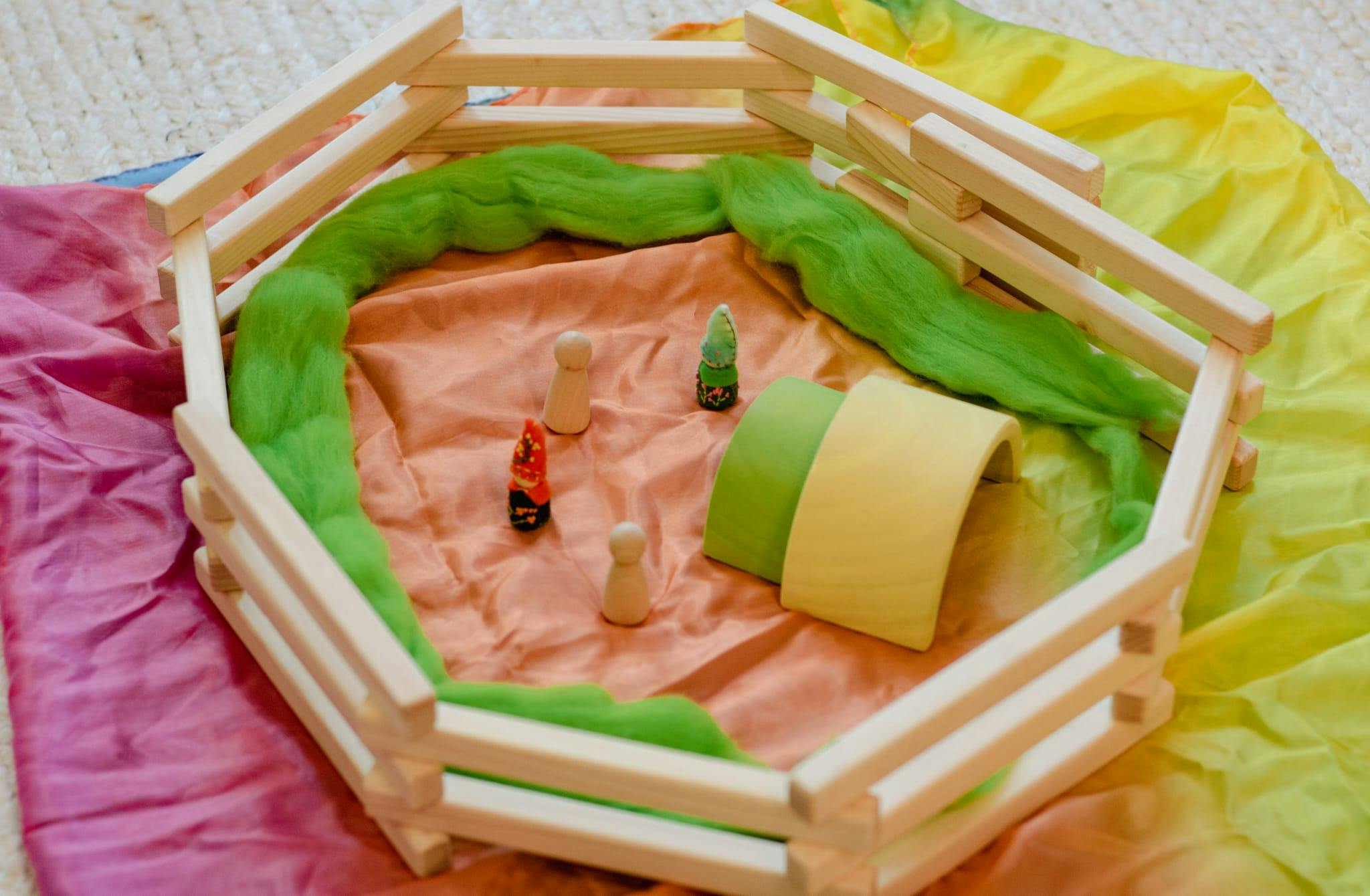 Wooden fence enclosing a play scene with fabric, small figures, and a tunnel