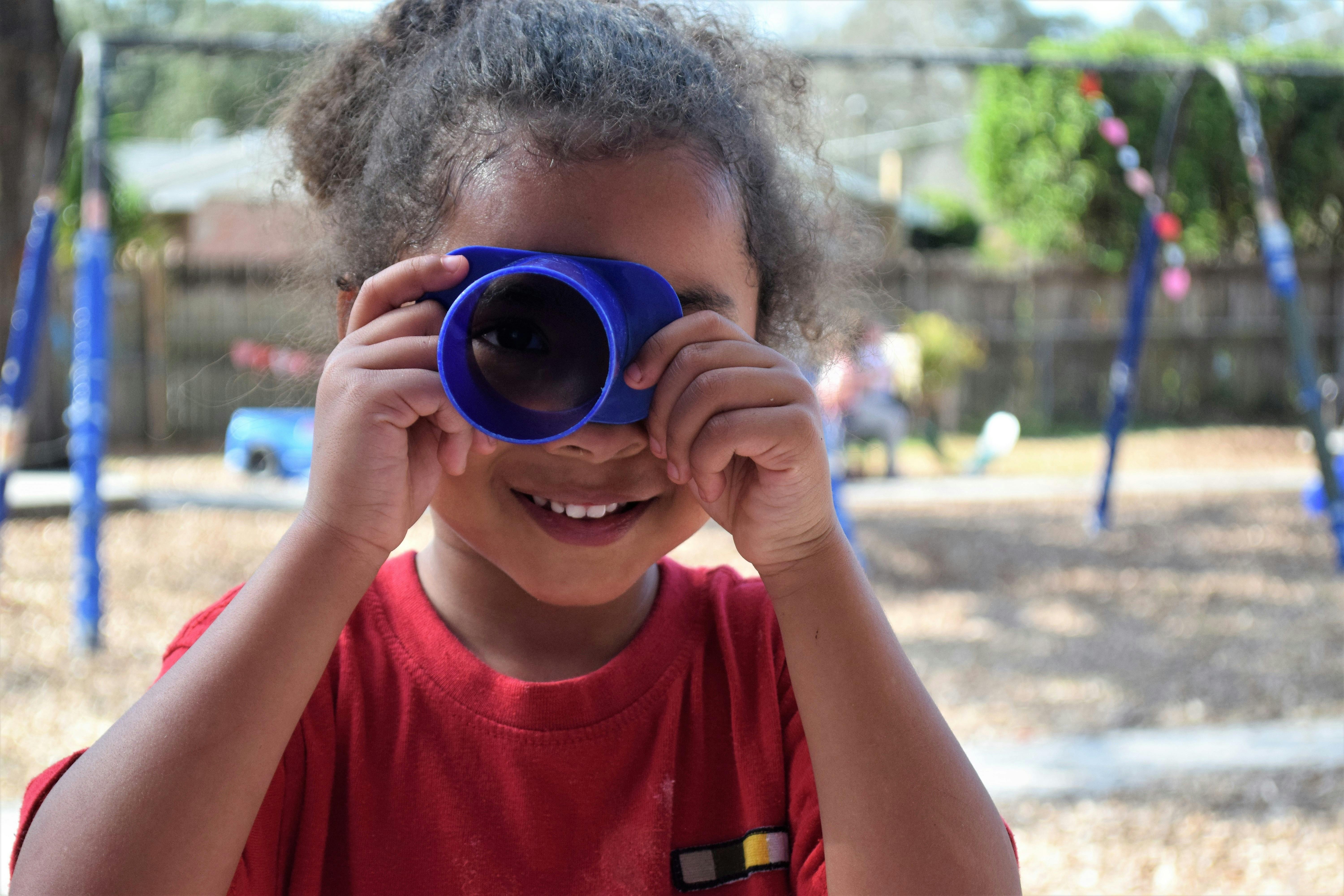Child looking through a blue plastic tube at a playground