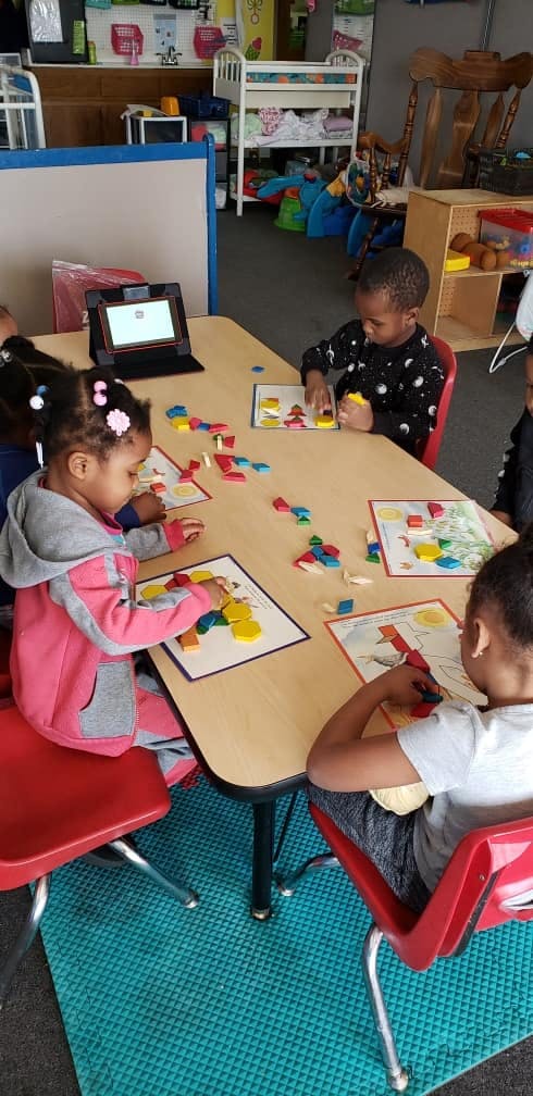 Three children at a table playing with colorful geometric shapes