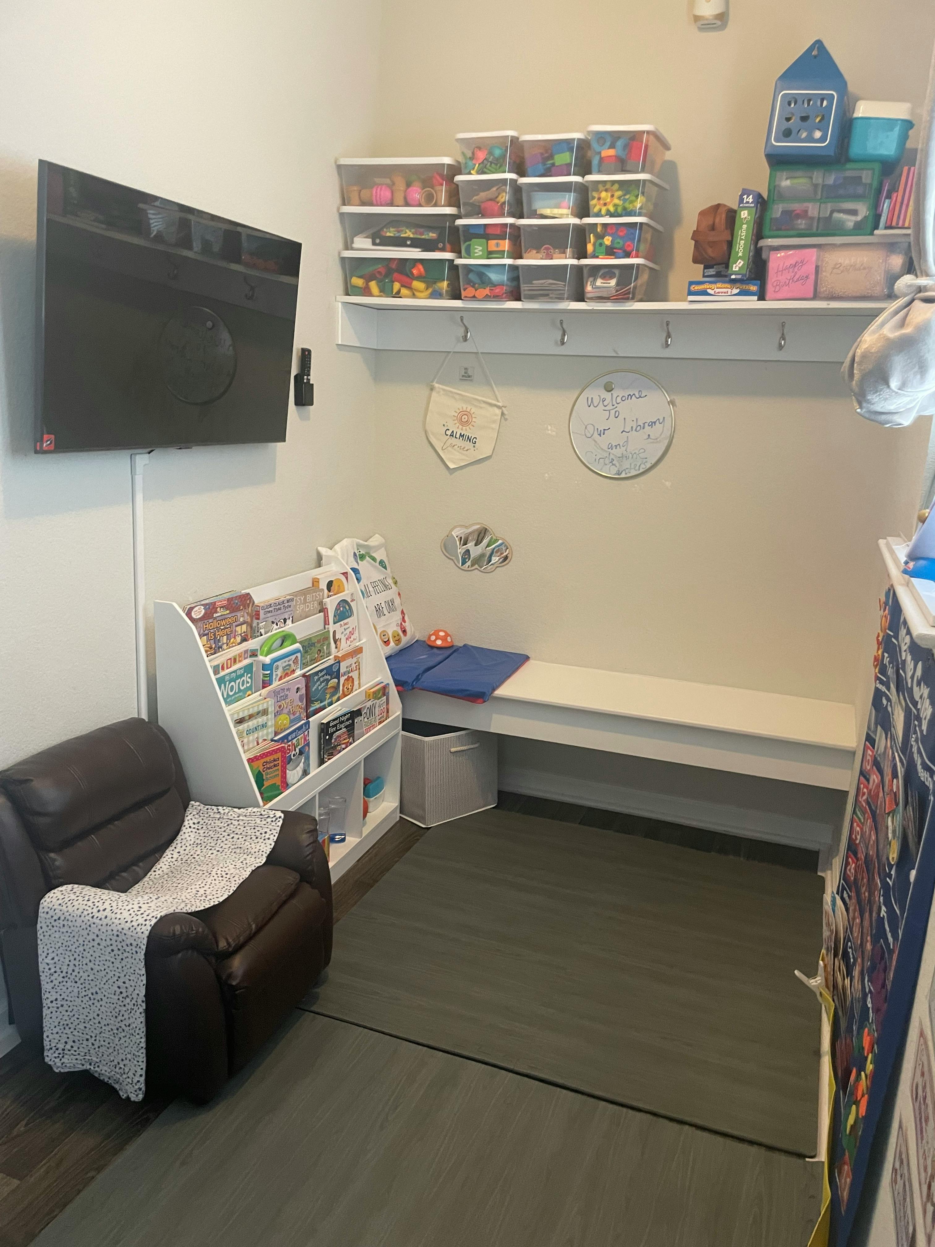 Room with a wall-mounted TV, bookshelf, recliner, and storage bench