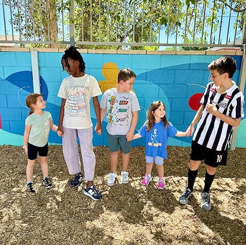 Five children standing in a row holding hands in front of a painted wall