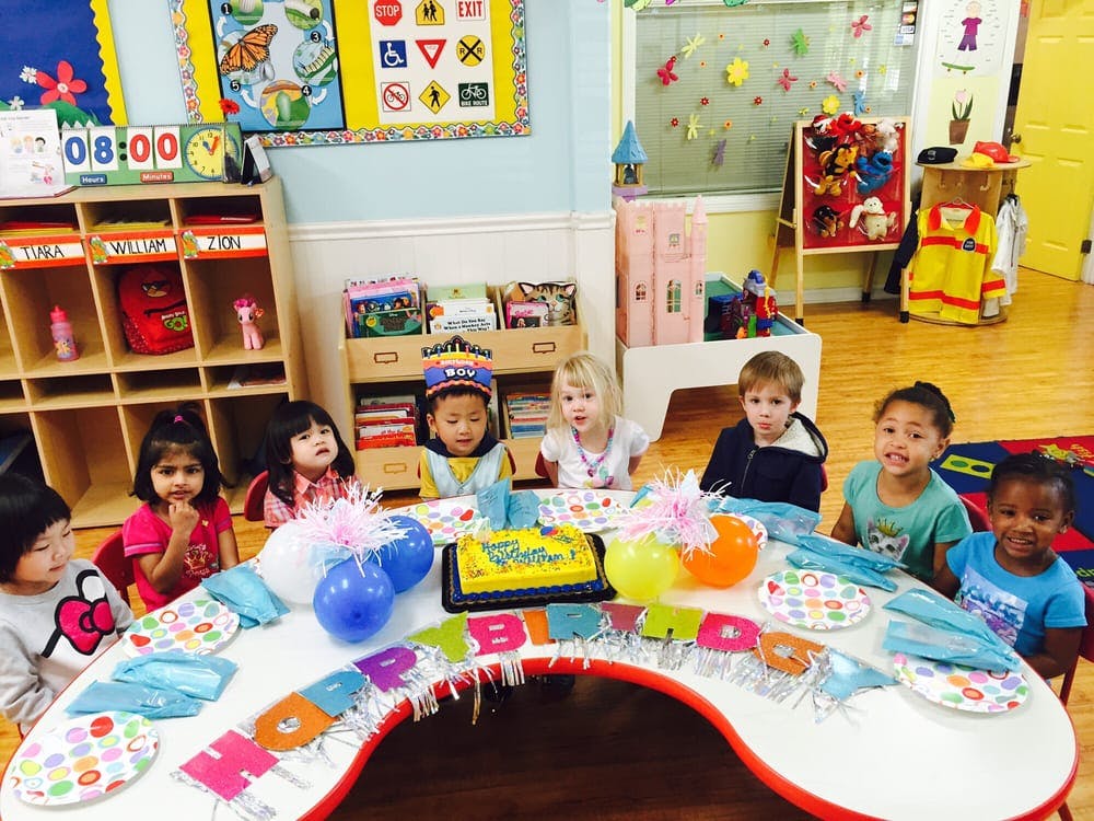 Children sitting around a table with a cake and balloons