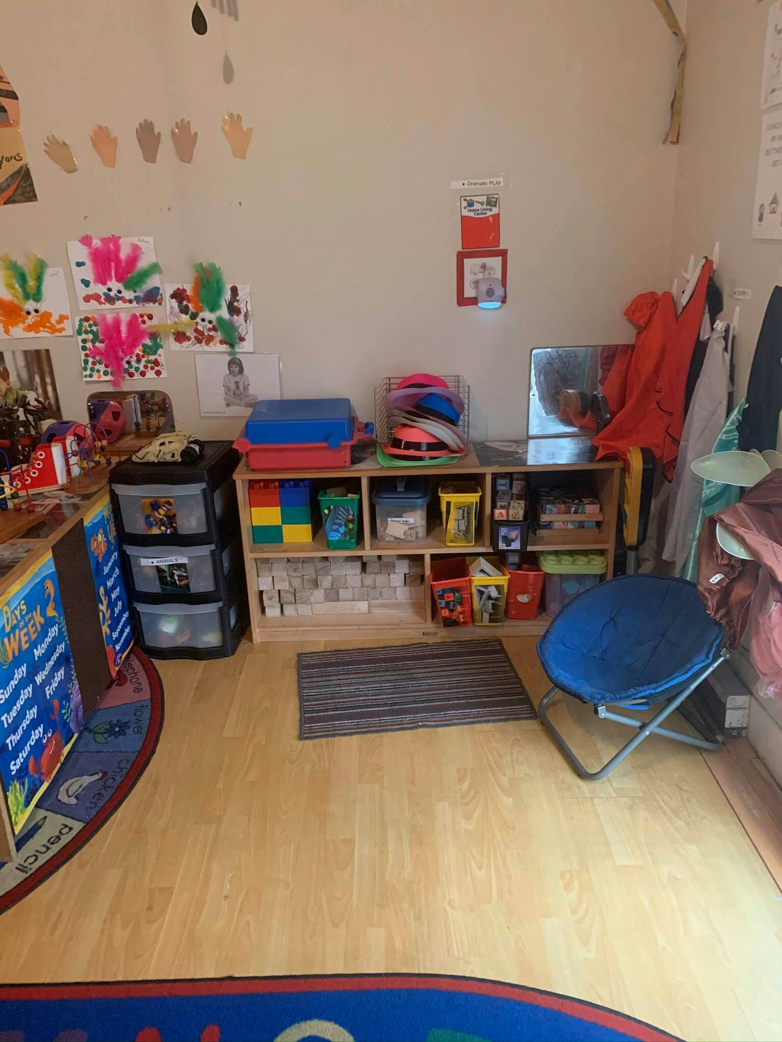 Classroom with shelves of toys, children's artwork on wall, and blue chair