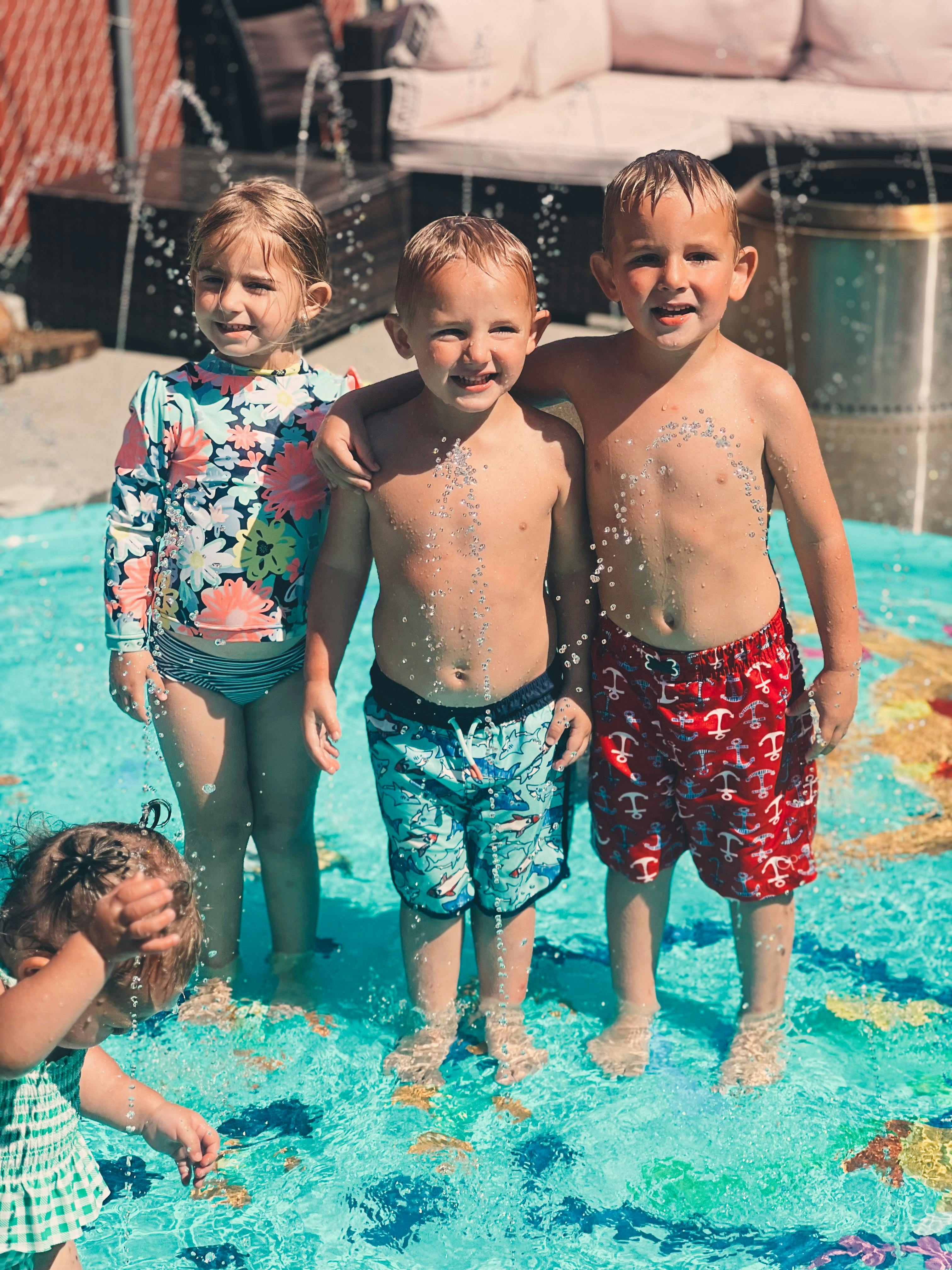 Three children standing in a shallow pool with water splashing