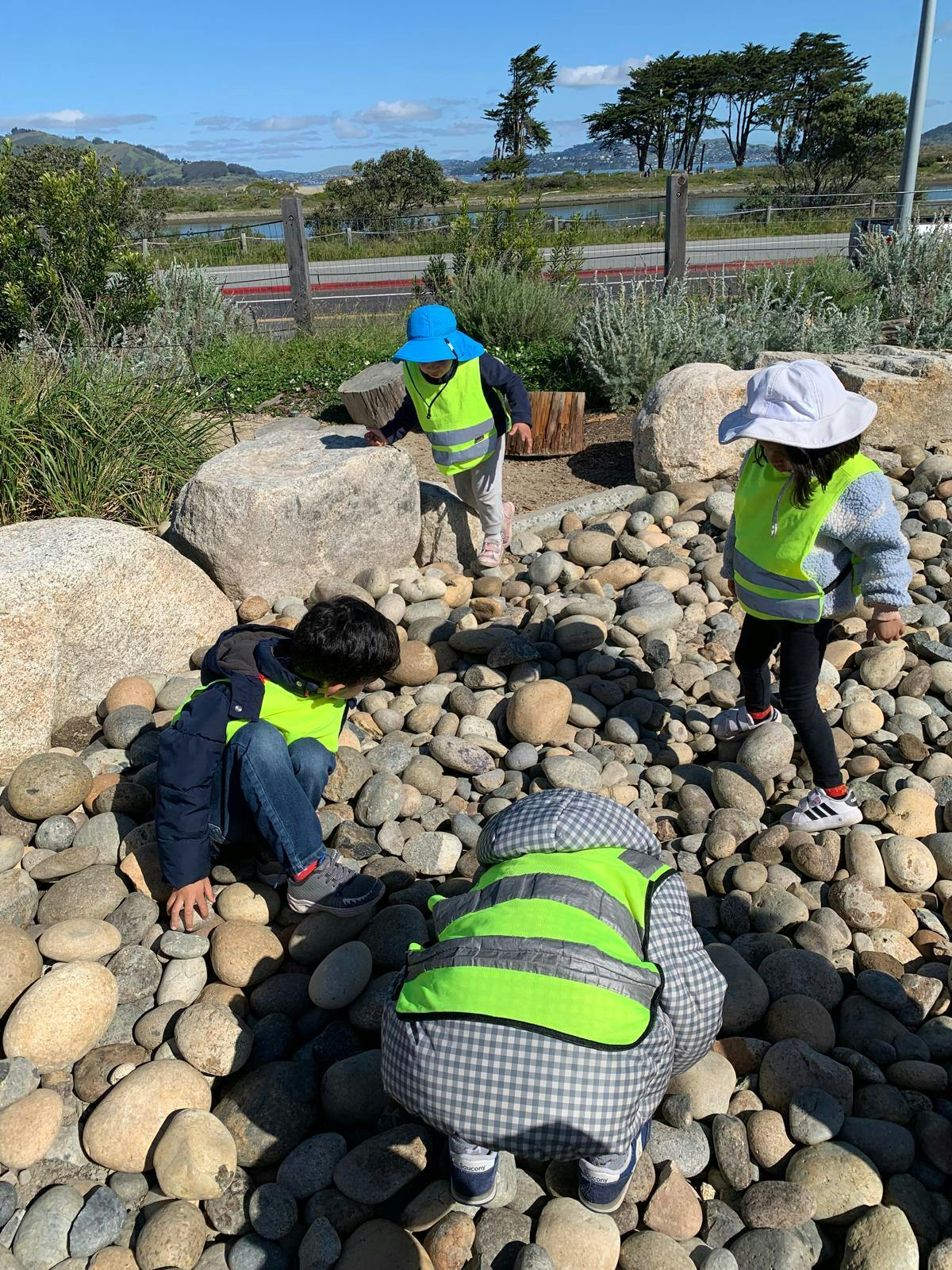 Four children in safety vests playing among rocks and boulders outdoors