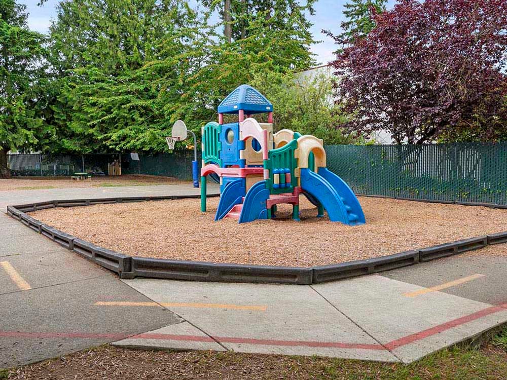 Colorful playground structure with slides on wood chips next to a paved area