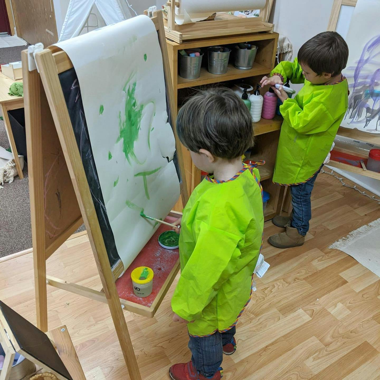 Two children painting at easels in a classroom