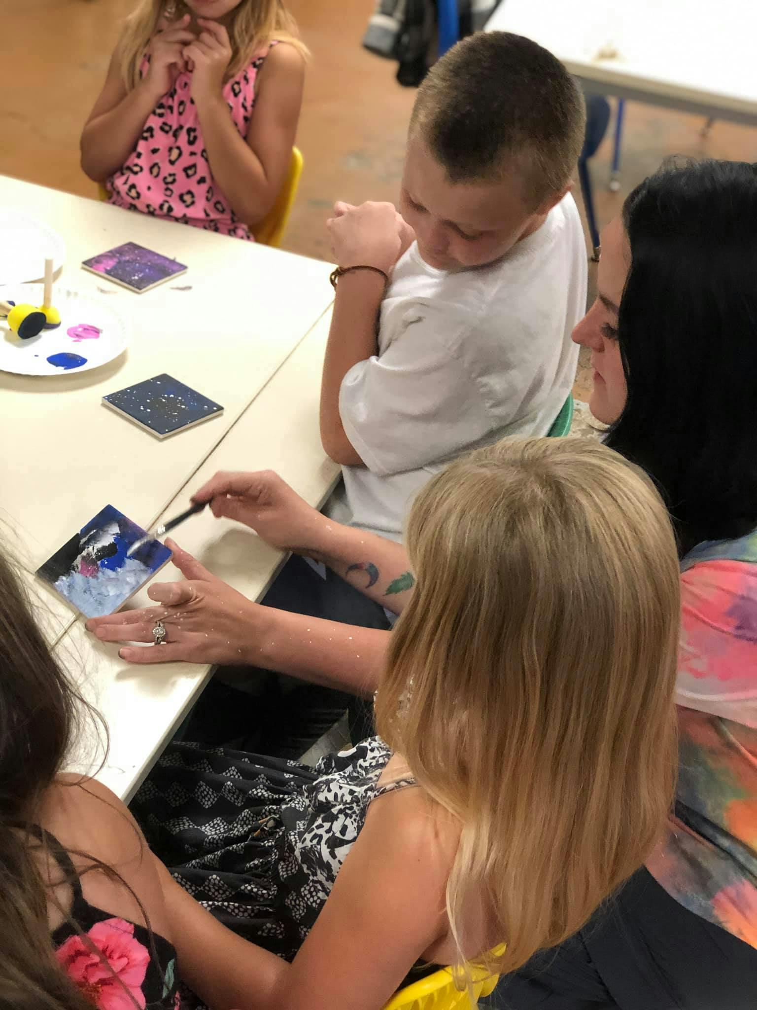 Person painting a small canvas with children watching