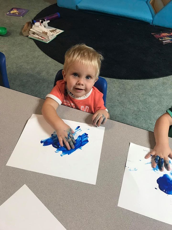 Child finger painting with blue paint on white paper
