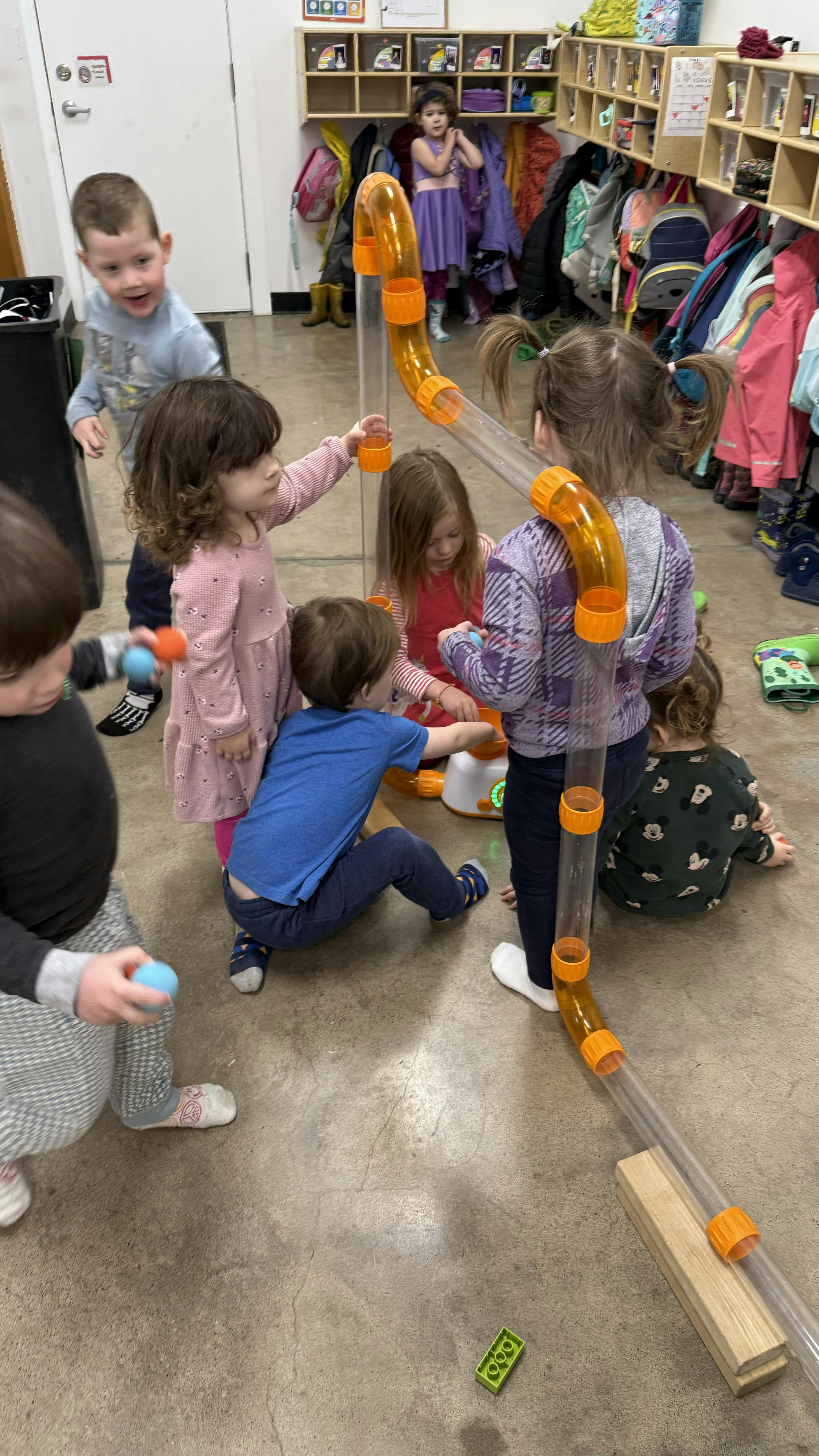 Several children playing with a clear tube structure in a classroom
