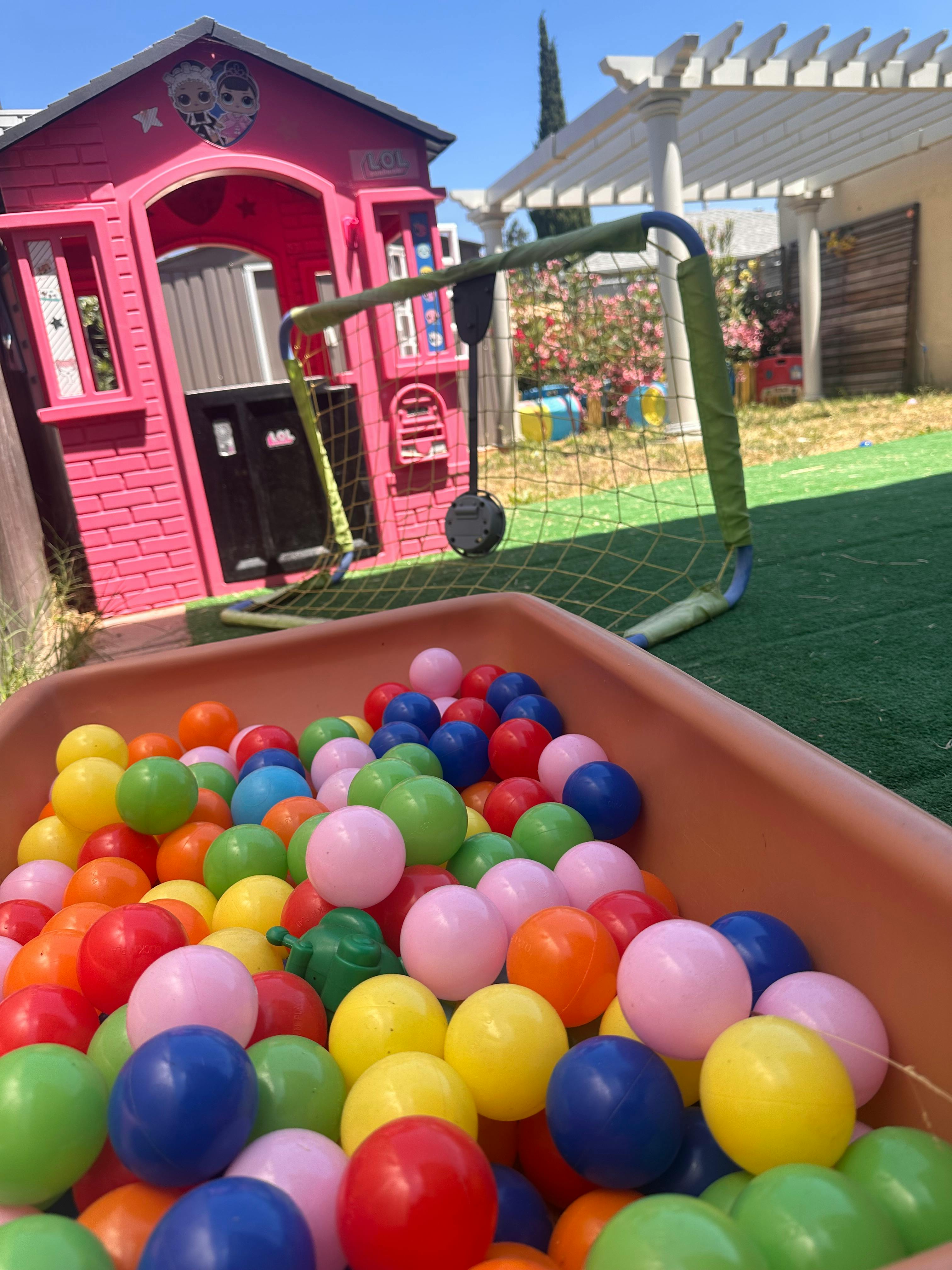 Colorful plastic balls in a bin with a pink playhouse and soccer goal in the background