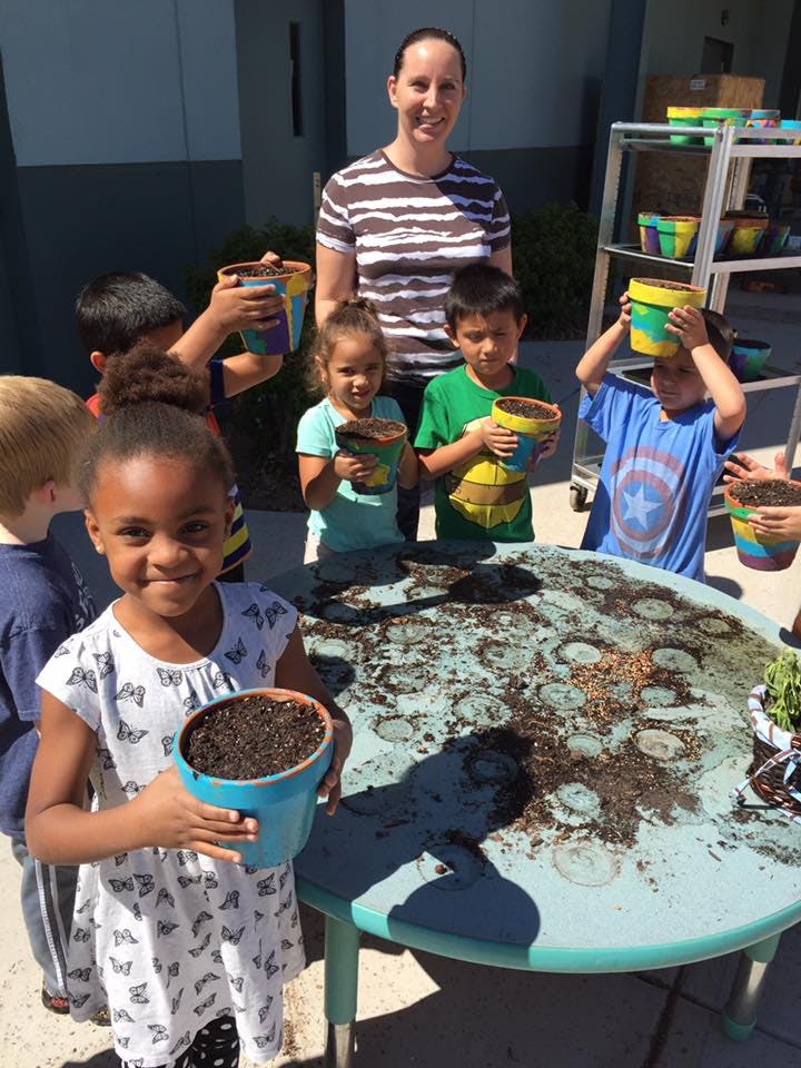 Adult and children holding potted plants around a table with soil