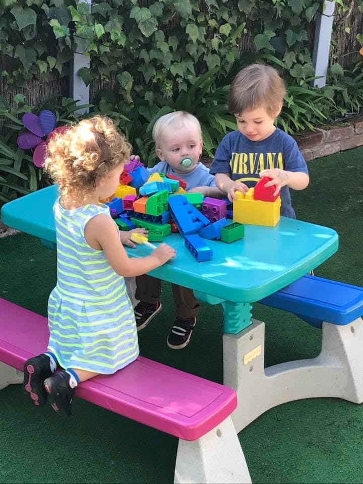 Three children playing with colorful building blocks at a small table
