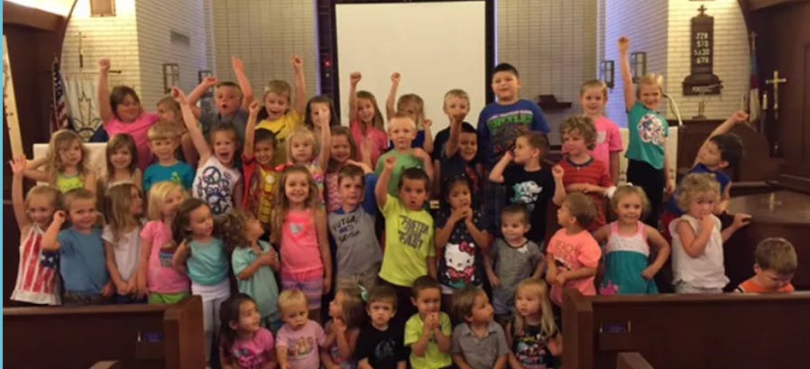 Group of children with some raising their hands in a room