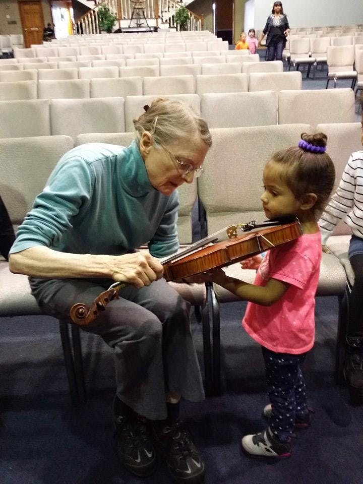 Person helping a child hold a violin