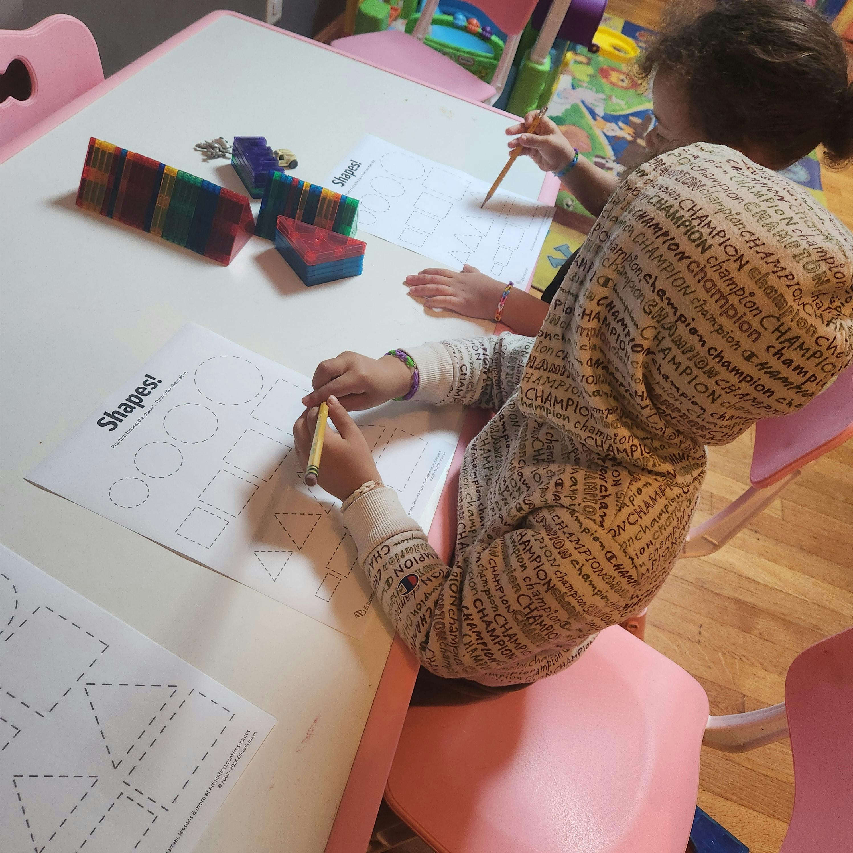 Child tracing shapes on a worksheet at a table