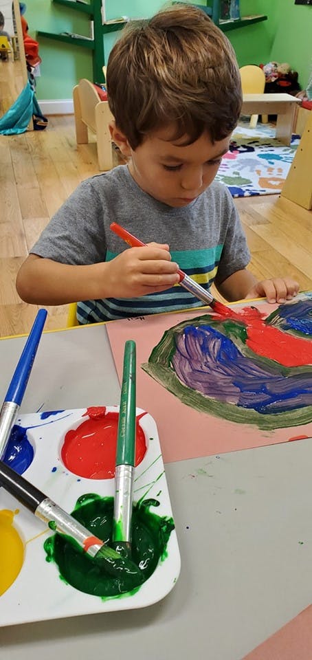 Child painting with a brush and colorful paints in a classroom