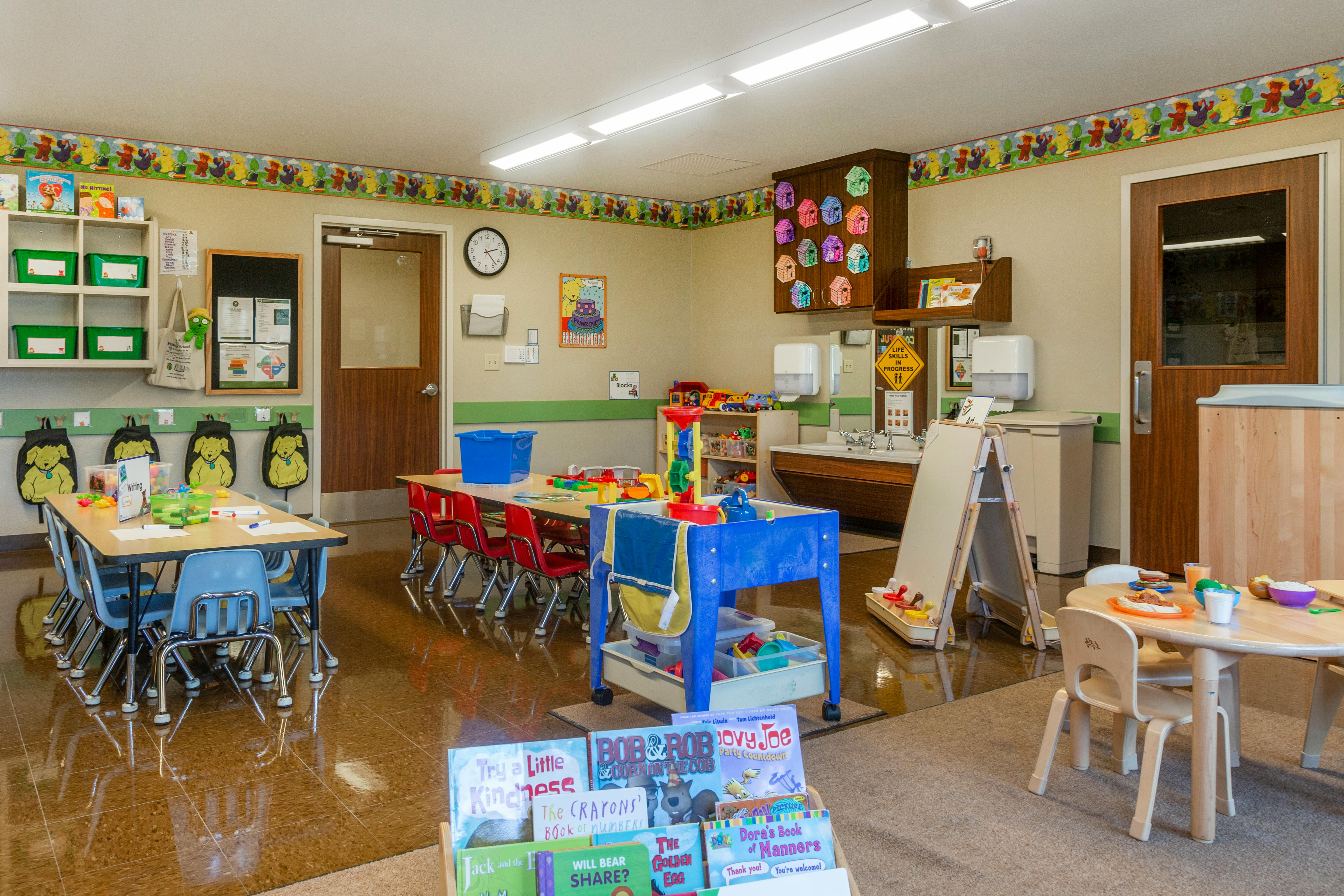 Classroom with child-sized tables and chairs, shelves, and a sink area
