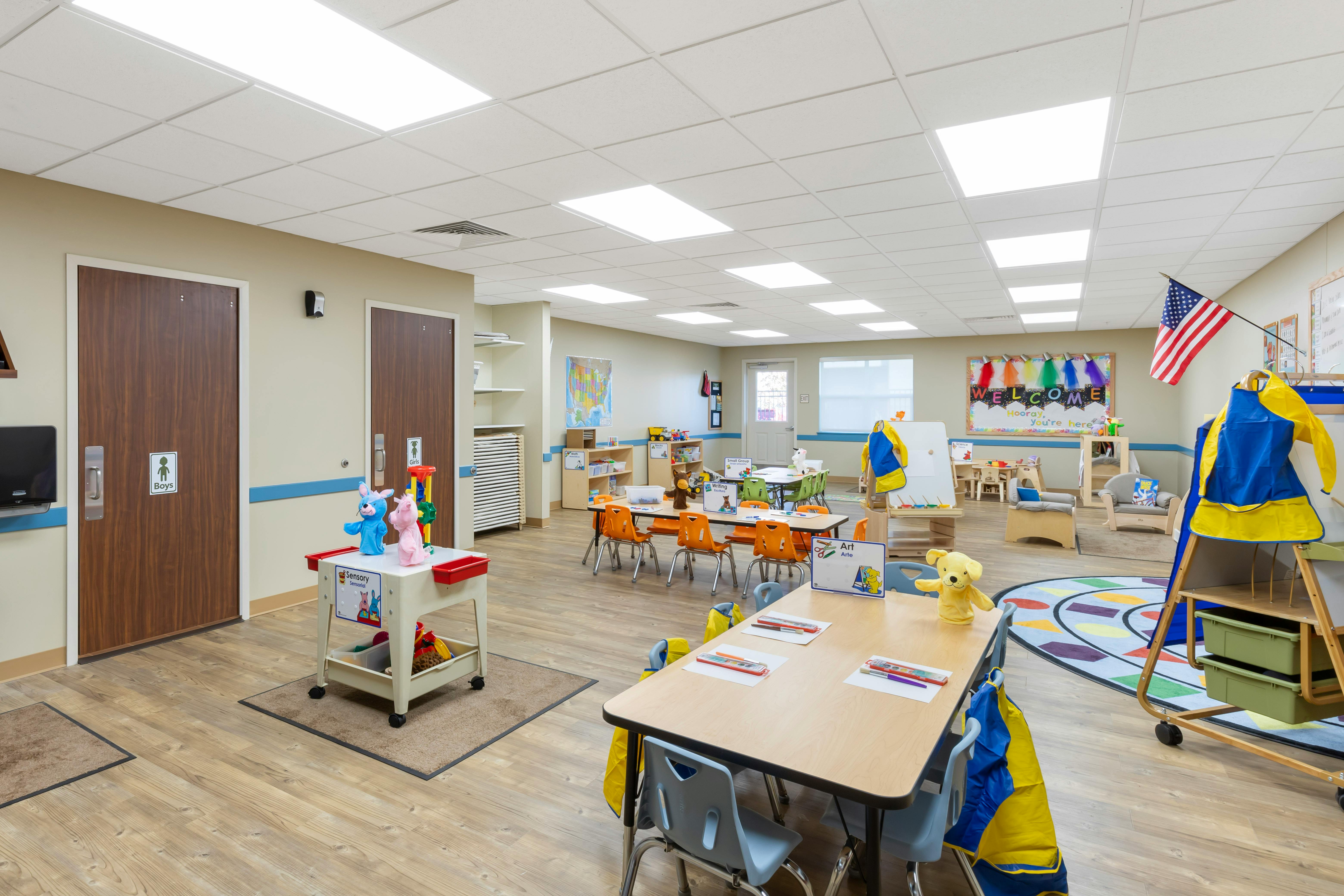 An empty early childhood classroom with multiple tables and chairs, a sensory table