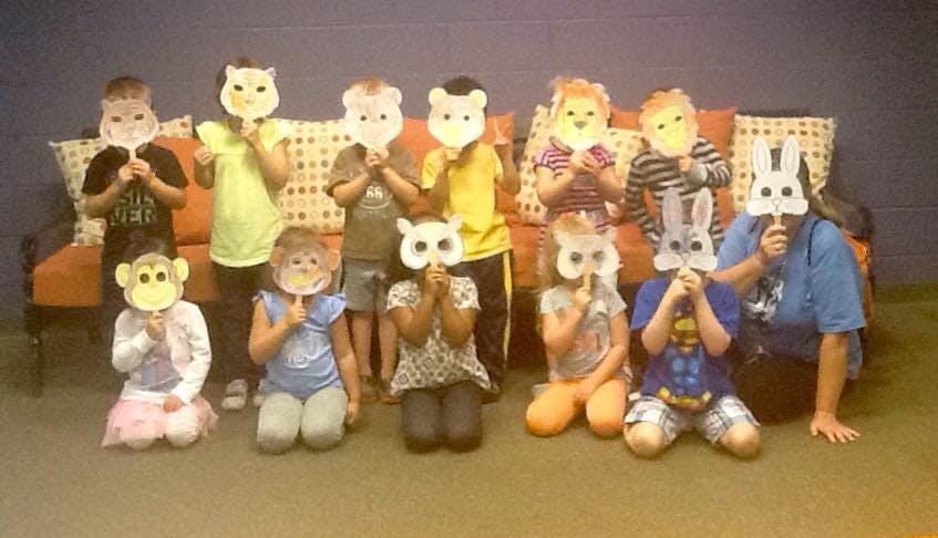 Group of children and an adult holding animal masks over their faces