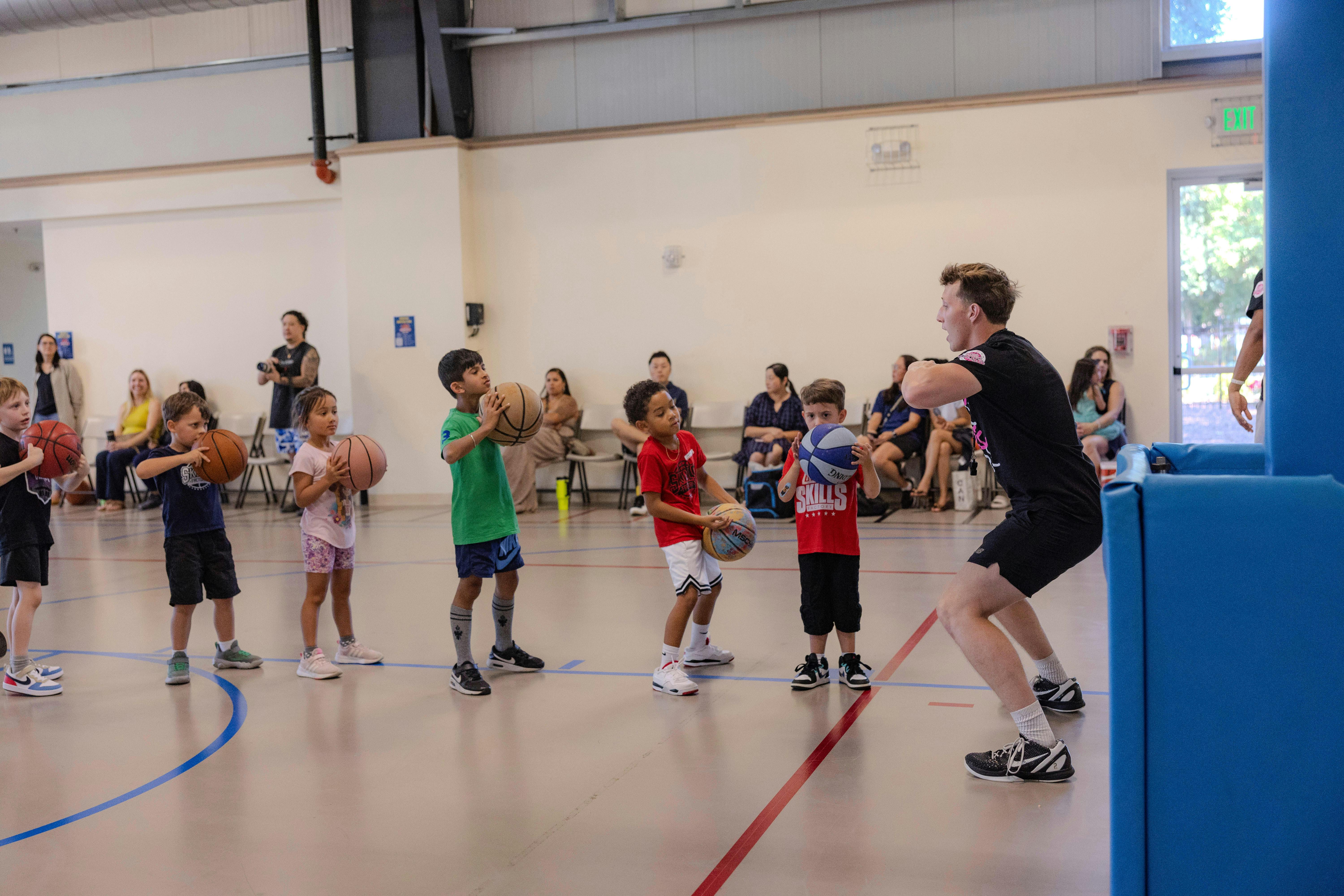 Adult teaching children how to play basketball in a gym